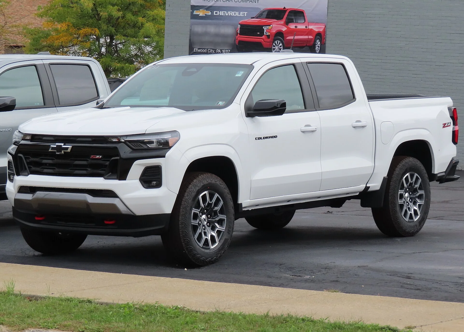 White Chevrolet Colorado Z71 crew-cab pickup on a dealer lot, front three-quarter view showing its black grille, Z71 badging, cargo bed, and off-road tires