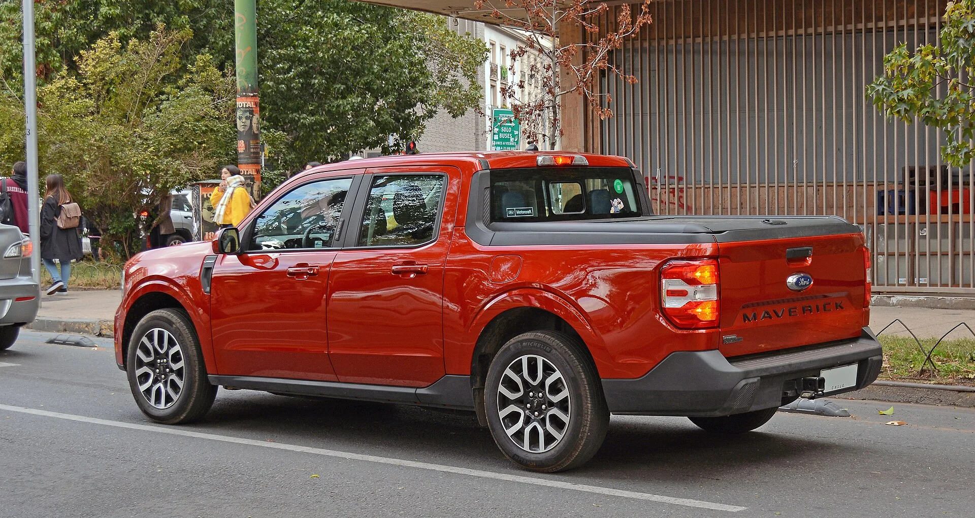Red Ford Maverick Hybrid Lariat compact pickup, rear three-quarter view showing the bed used for payload