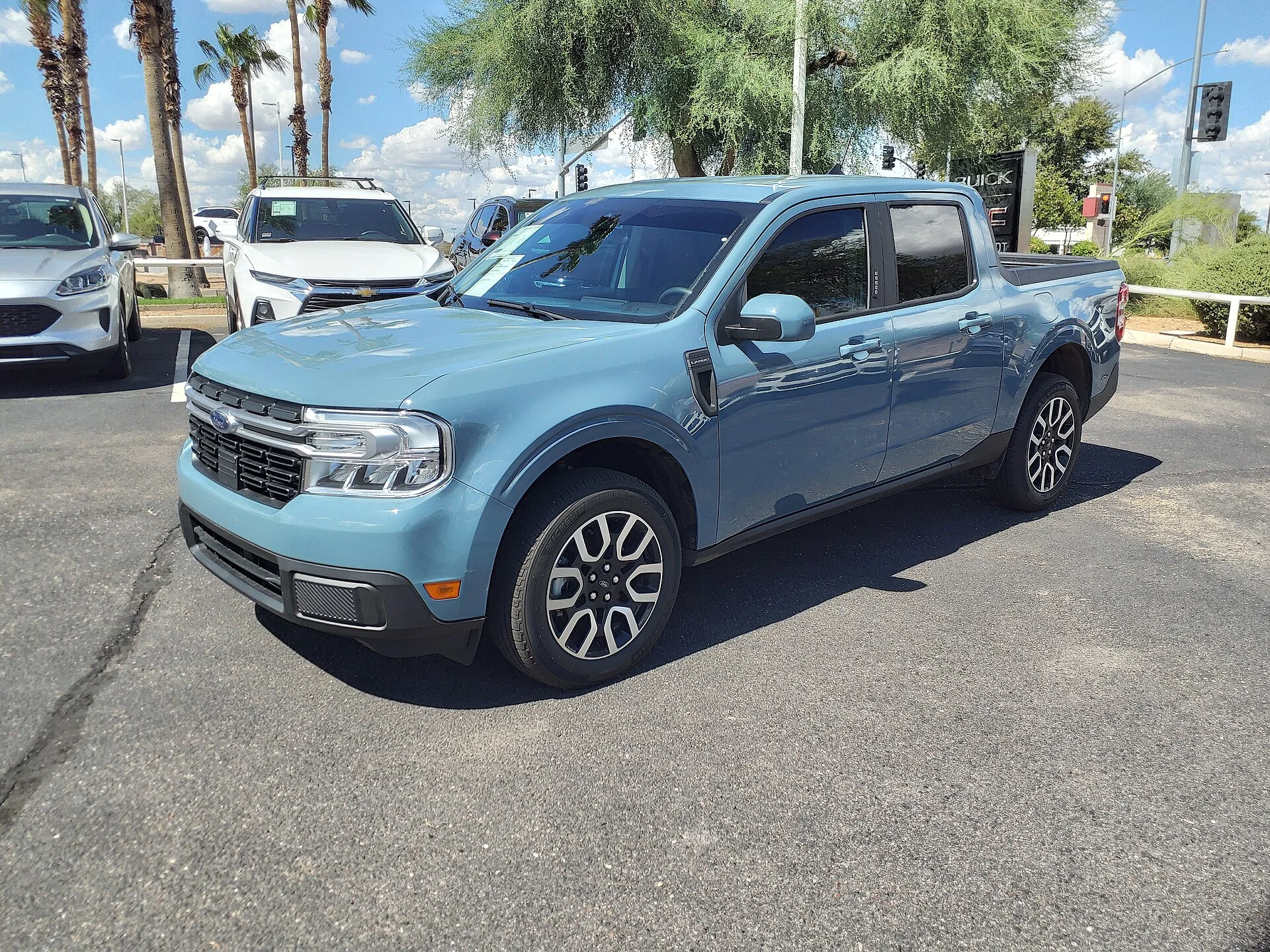 Light blue Ford Maverick Lariat crew-cab pickup, front three-quarter view showing the Ford grille and open cargo bed on a dealer lot
