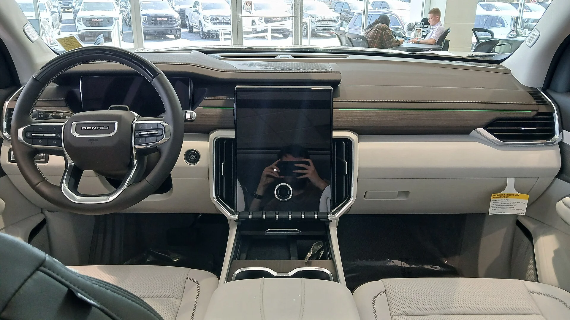 The interior of a current GMC Acadia Denali showing the dashboard, steering wheel, vertical touchscreen and light-coloured seats.