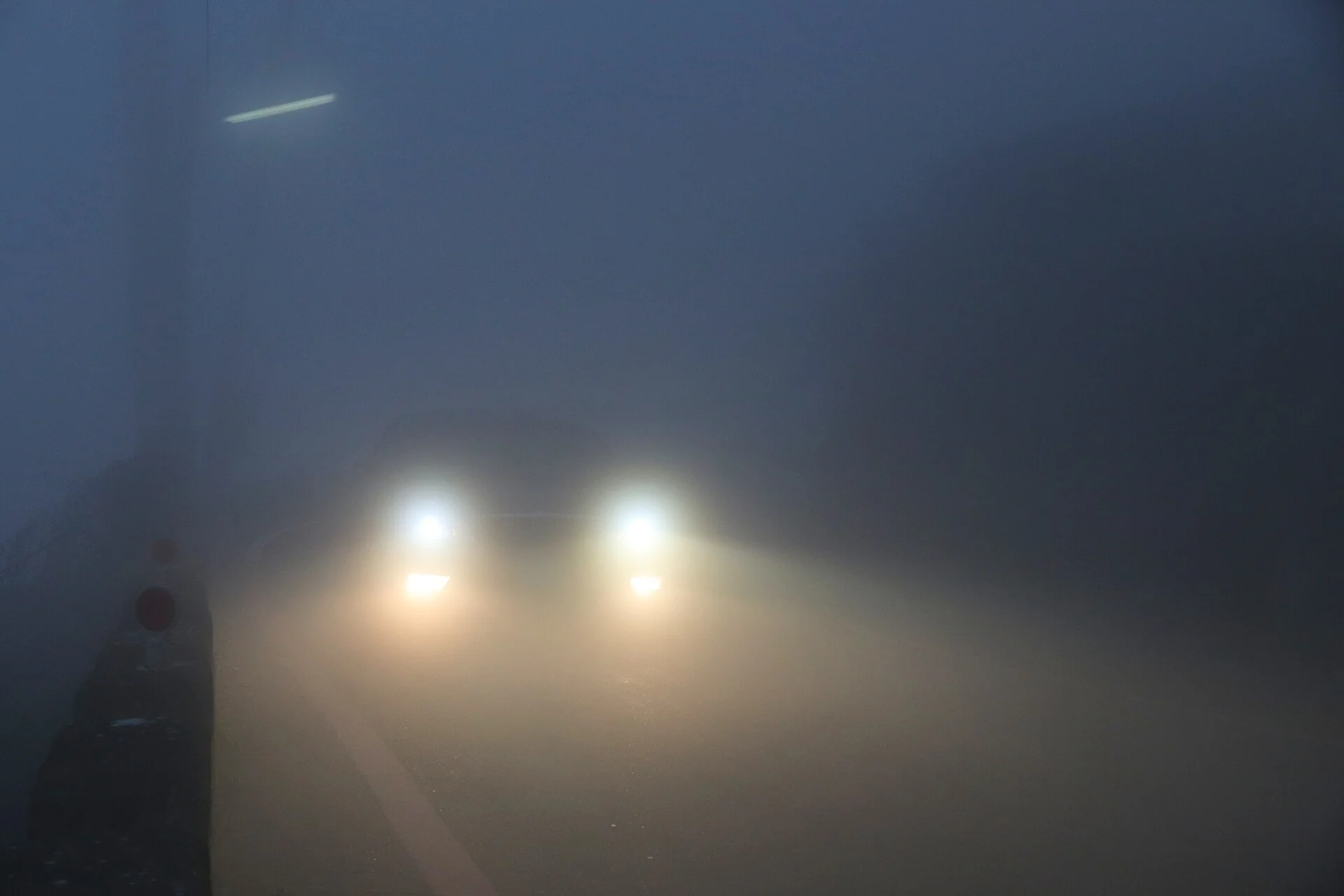 Car driving through dense fog — the low-visibility conditions where drivers wonder if hazard lights are legal