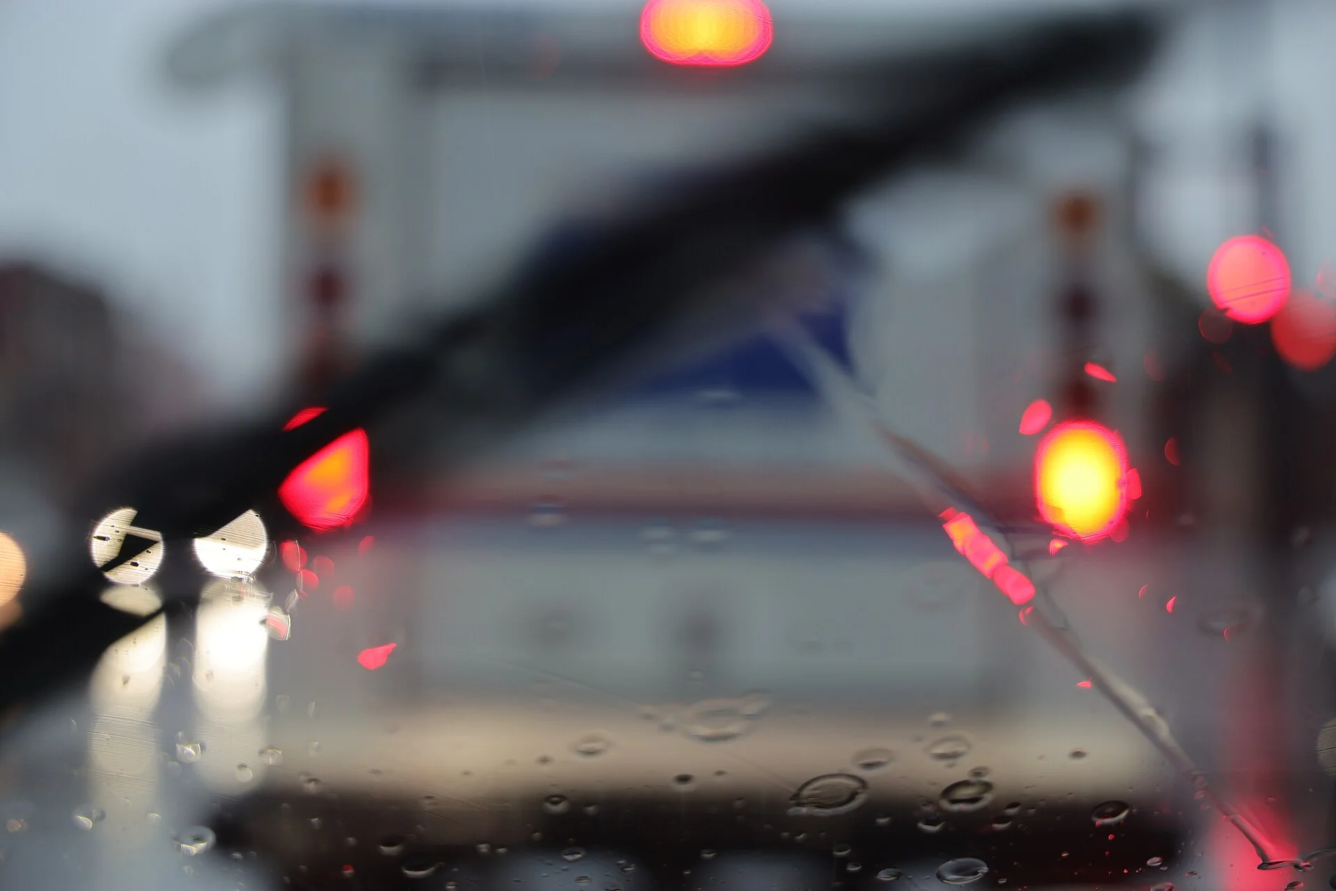 The view through a rain-covered windshield in slow traffic, the red brake and hazard lights of vehicles ahead glowing in the downpour — the low-visibility rain conditions this hazard-lights guide addresses.