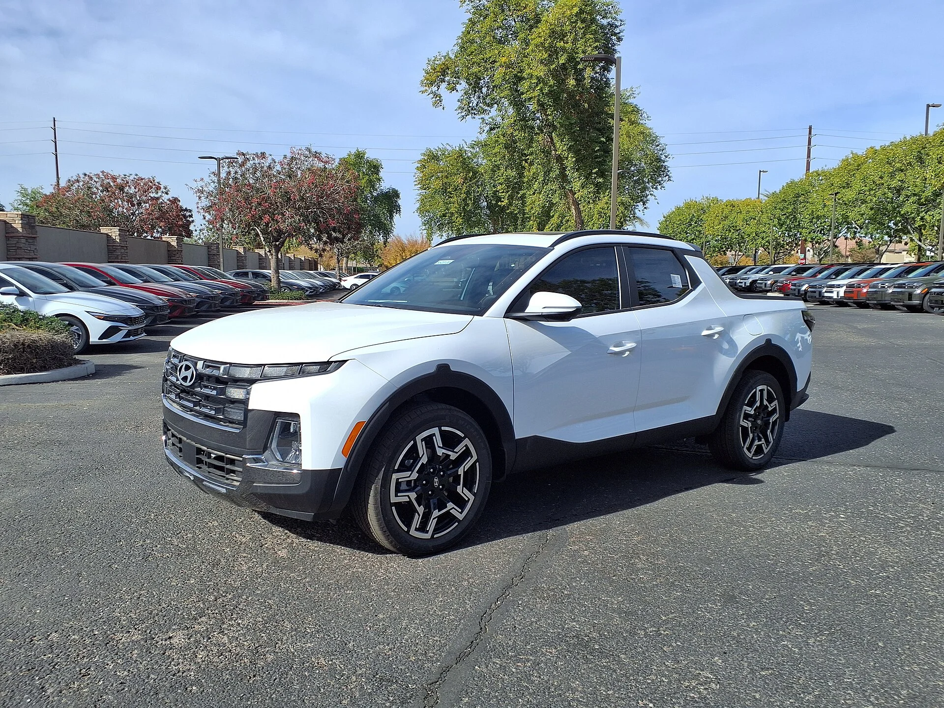 White Hyundai Santa Cruz compact pickup at a dealer lot, front three-quarter view showing its short cargo bed, alloy wheels, and Hyundai grille