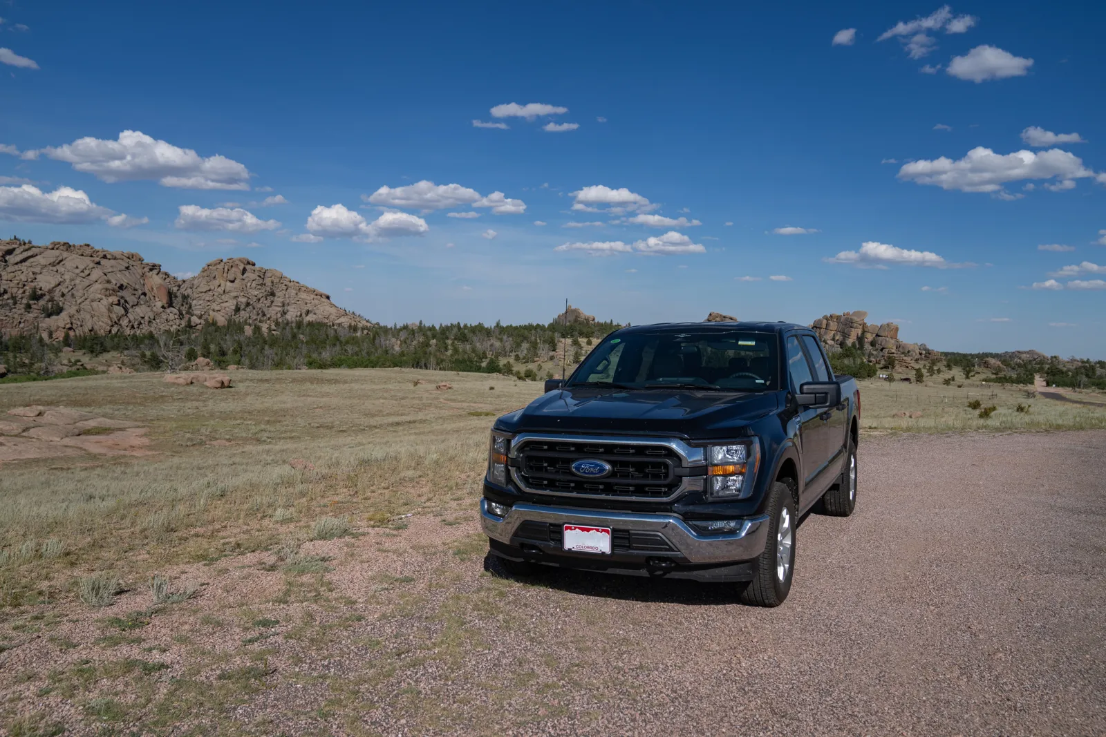 Dark-blue Ford F-150 crew-cab pickup truck, current generation, parked on a gravel road in the Wyoming mountains under a blue sky.