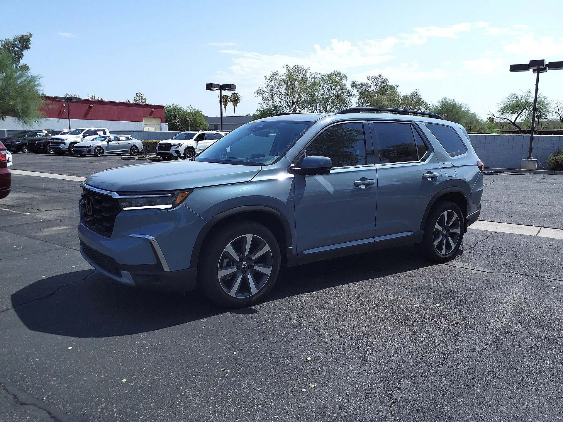 Sage-blue Honda Pilot SUV in a parking lot, front three-quarter view showing its roof rails, alloy wheels, and Honda grille