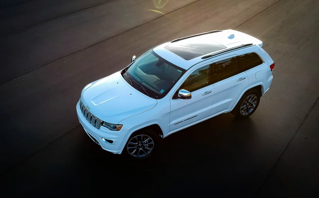 White Jeep Grand Cherokee SUV with a sunroof, elevated front three-quarter view showing the seven-slot Jeep grille and alloy wheels