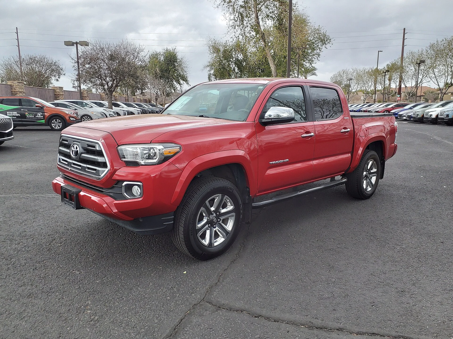 Red third-generation (2016-2023) Toyota Tacoma Limited double-cab pickup, front three-quarter view on a dealer lot, showing the chrome hexagonal grille with Toyota badge, projector headlights and TACOMA embossed on the bedside