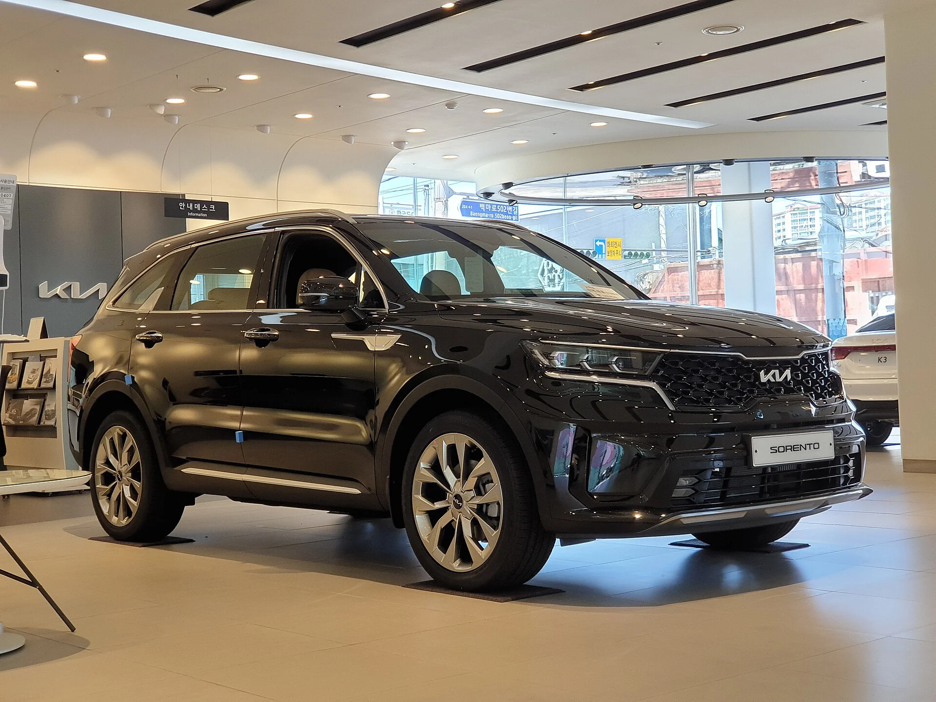 Black Kia Sorento SUV, front three-quarter view with the tiger-nose grille and machined-alloy wheels, on display in a showroom.