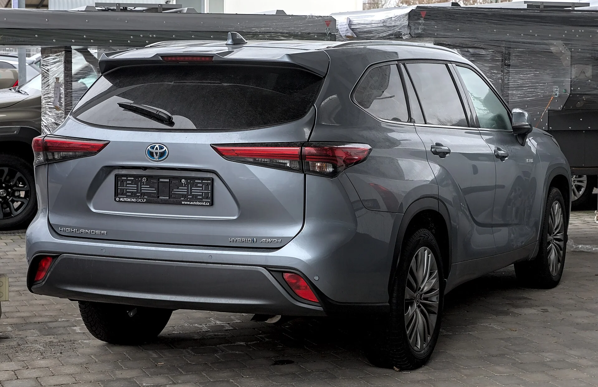 Gray Toyota Highlander Hybrid SUV, rear three-quarter view showing the HIGHLANDER and HYBRID AWD-i badges.