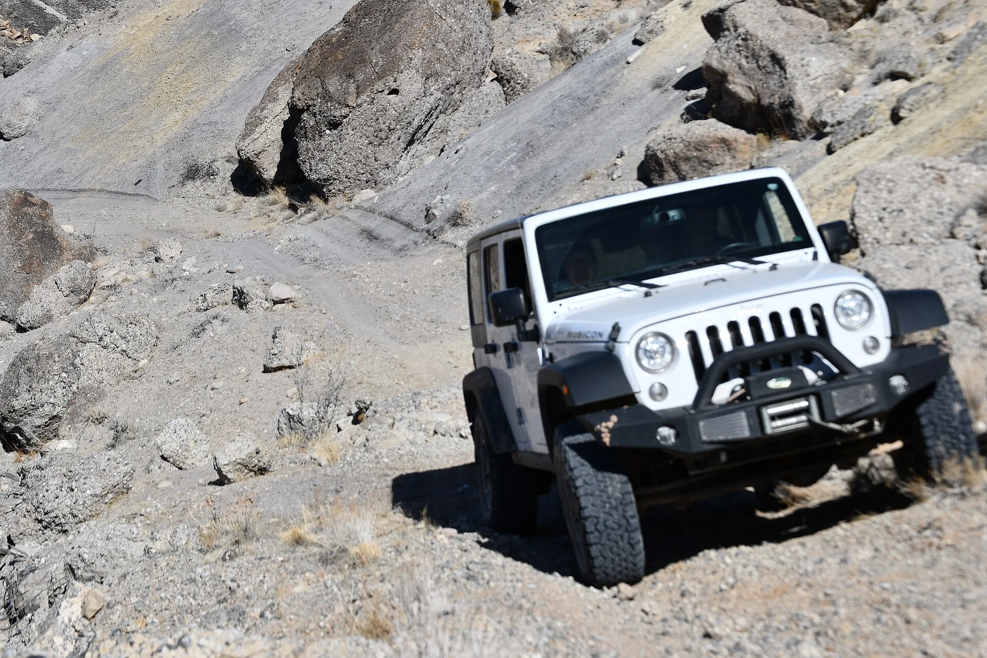 White Jeep Wrangler climbing a rocky off-road trail, showing high ground clearance for overlanding