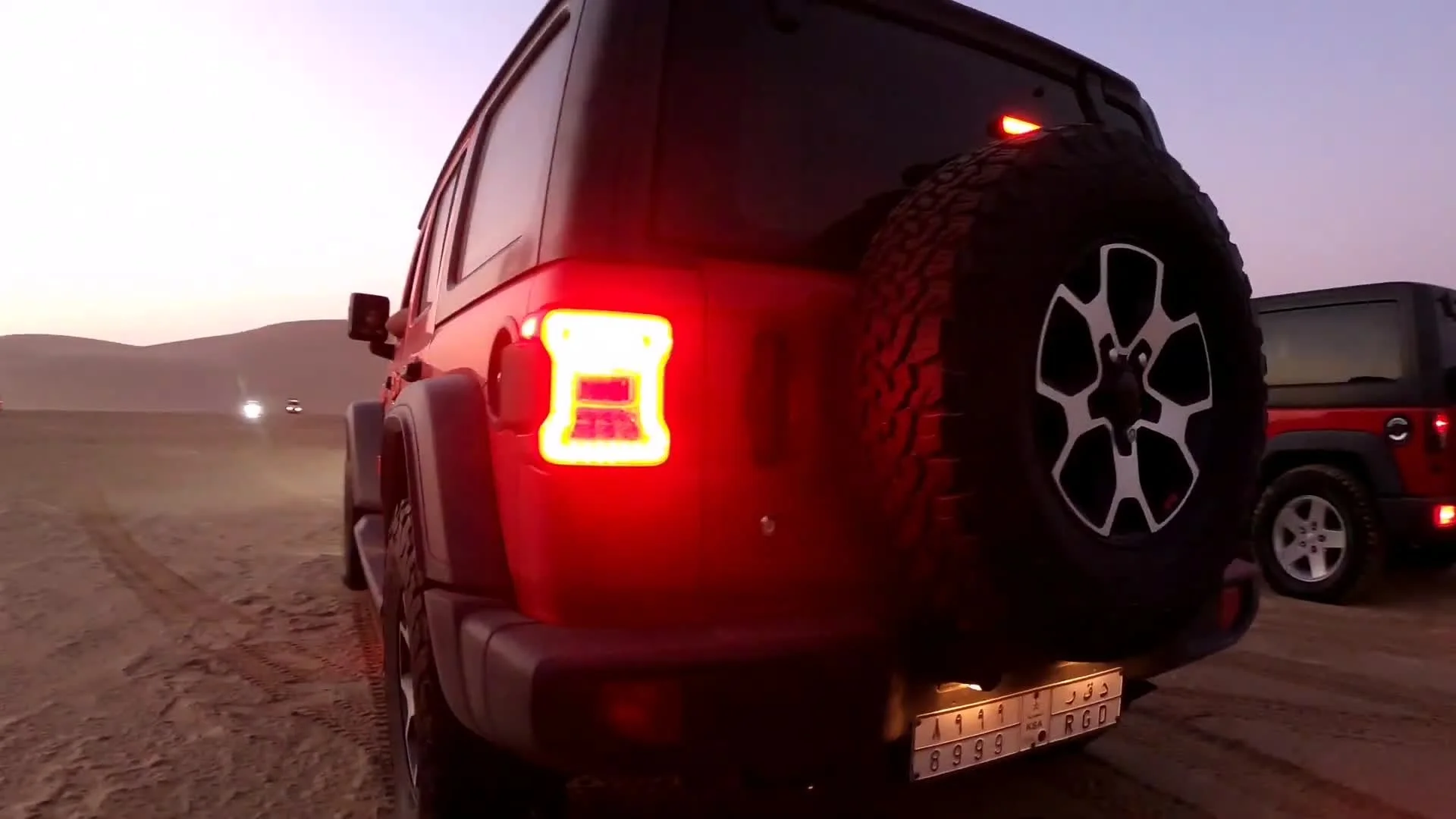 Black Jeep Wrangler Rubicon on desert sand, rear view with brake lights lit