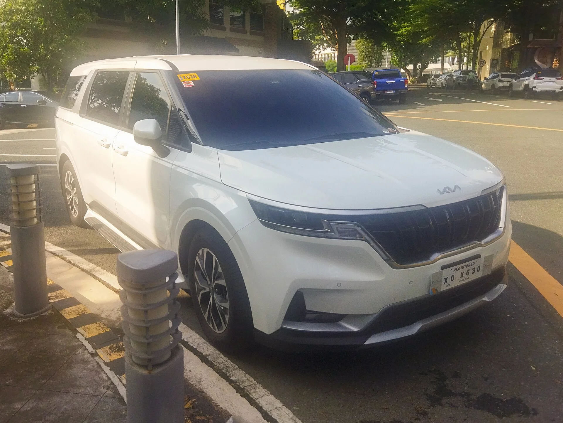 White Kia Carnival minivan, current KA4 generation, parked kerbside in a front three-quarter view.