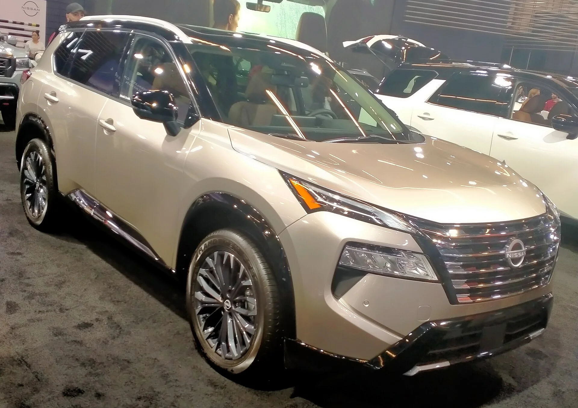 Champagne-gold 2024 Nissan Rogue compact SUV, current generation, on an auto-show stand in a front three-quarter view.