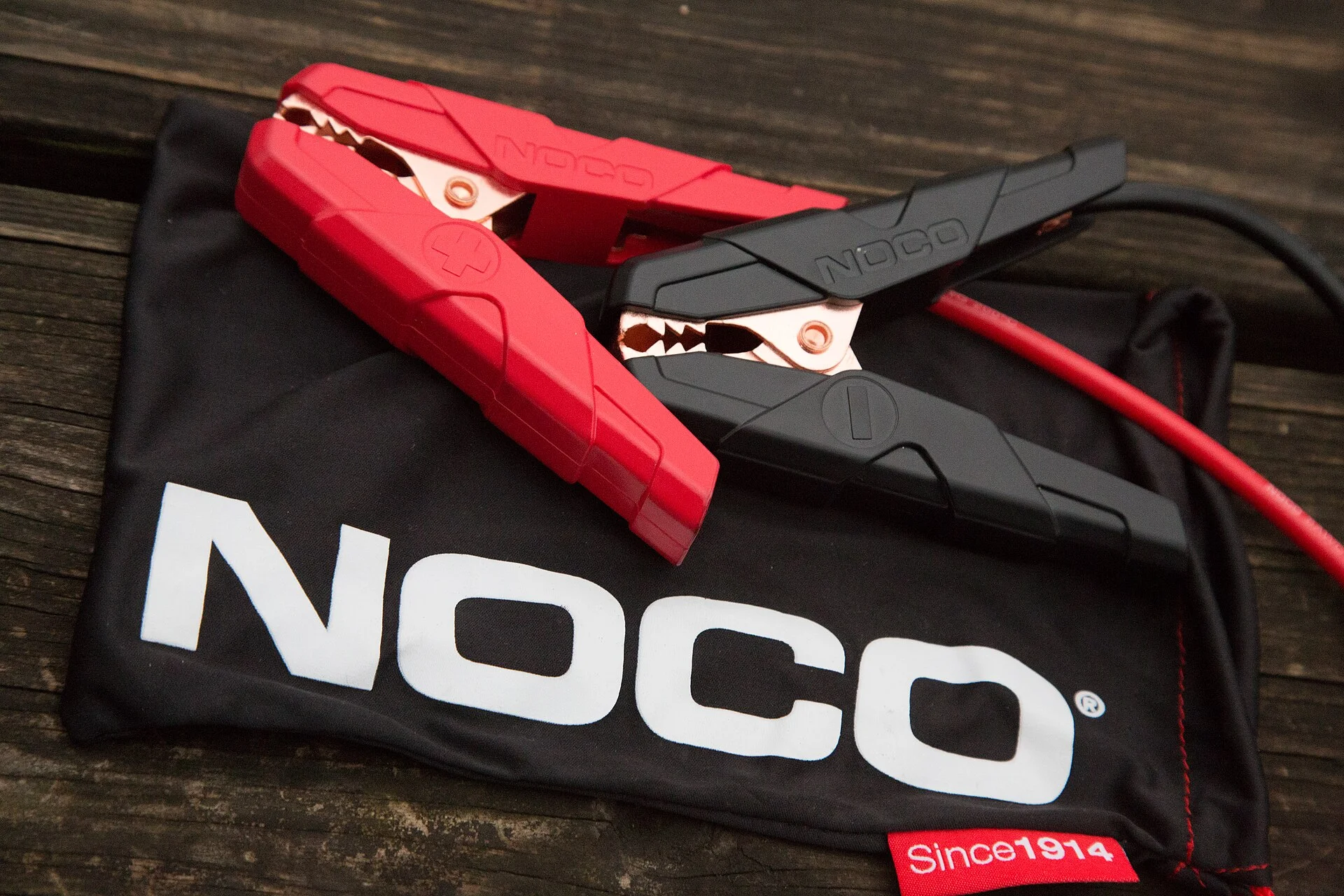 Red and black NOCO jumper-cable clamps resting on a branded storage pouch.