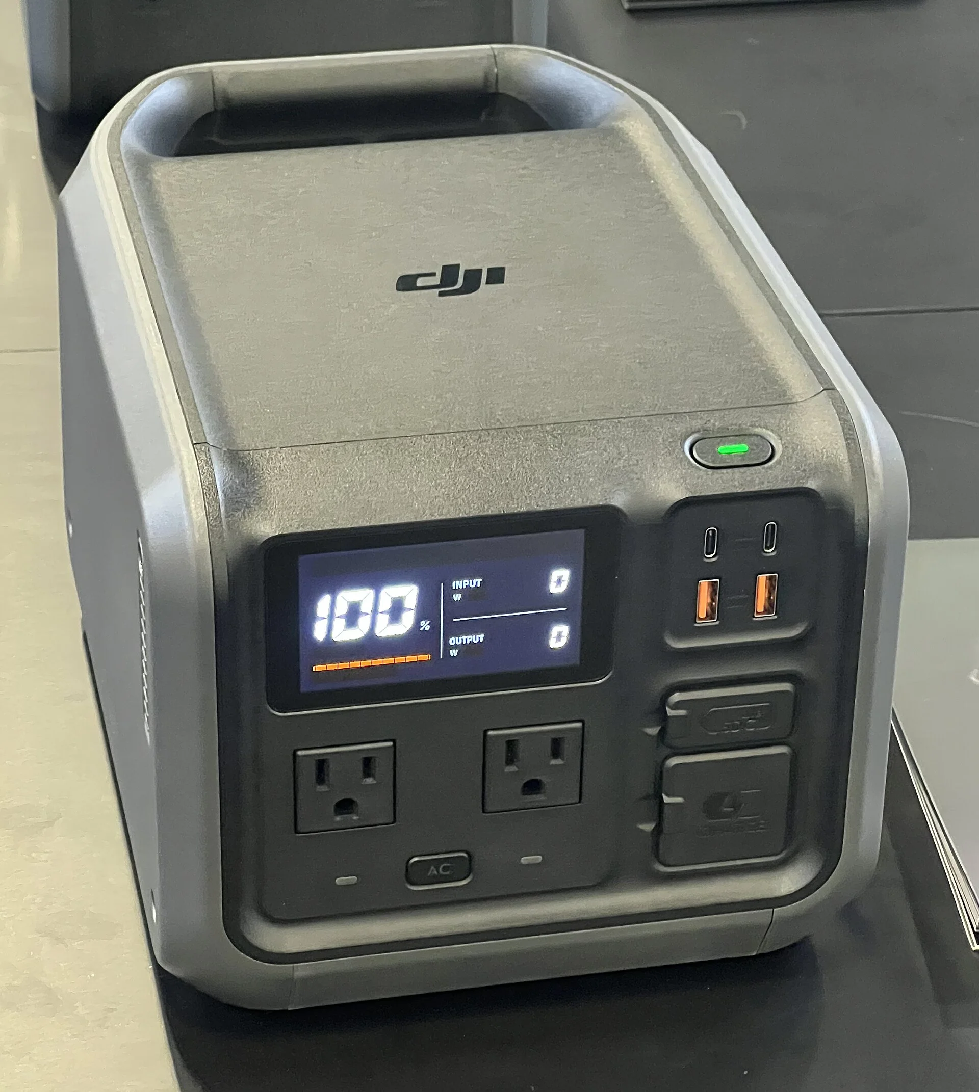 Dark grey DJI Power 500 portable power station, three-quarter view, its display reading 100 percent above two AC outlets and USB ports