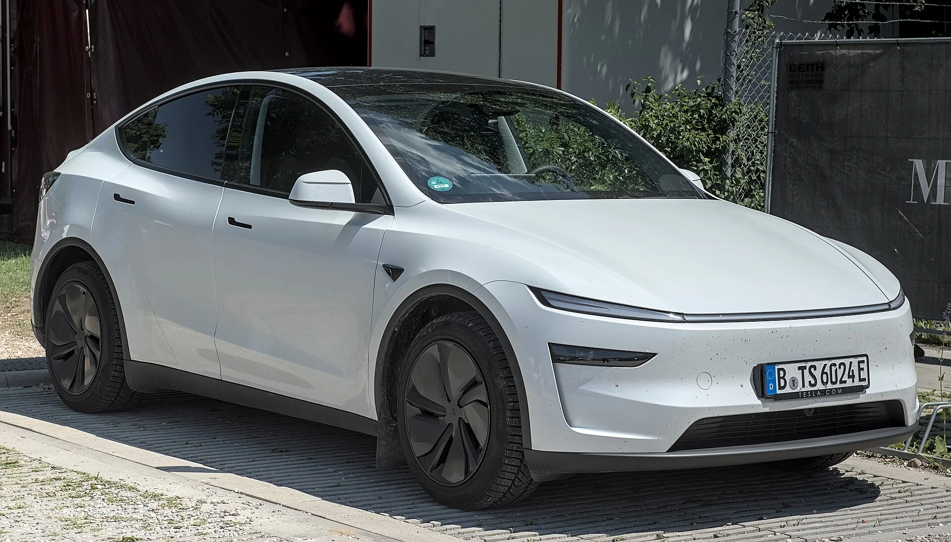 White Tesla Model Y electric SUV, current refreshed generation with its full-width front light bar, front three-quarter view.