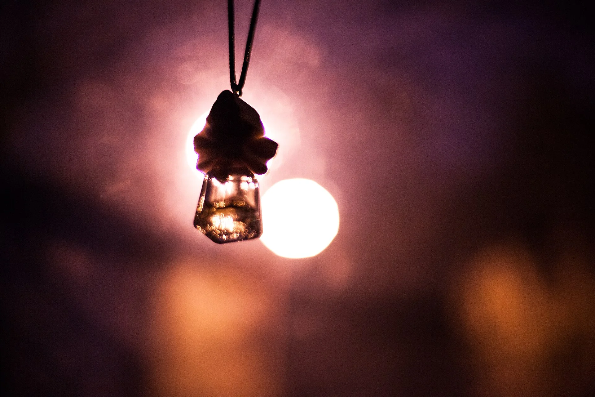 A tree-shaped disposable car air freshener hanging by a cord, silhouetted against warm evening light