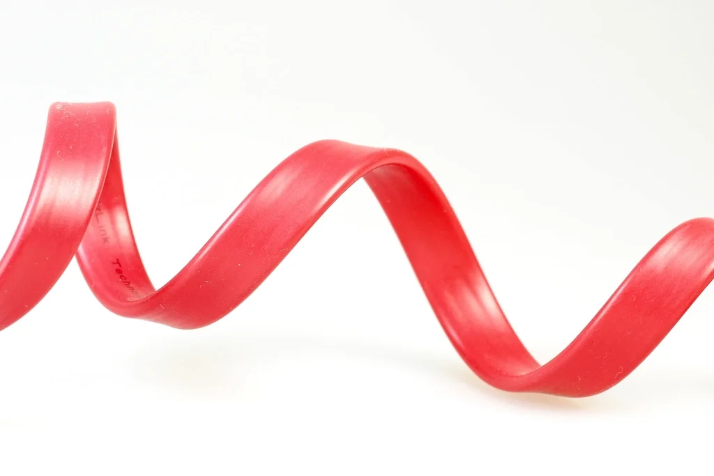 A flat red USB cable coiled on a white background, illustrating USB charging cabling.