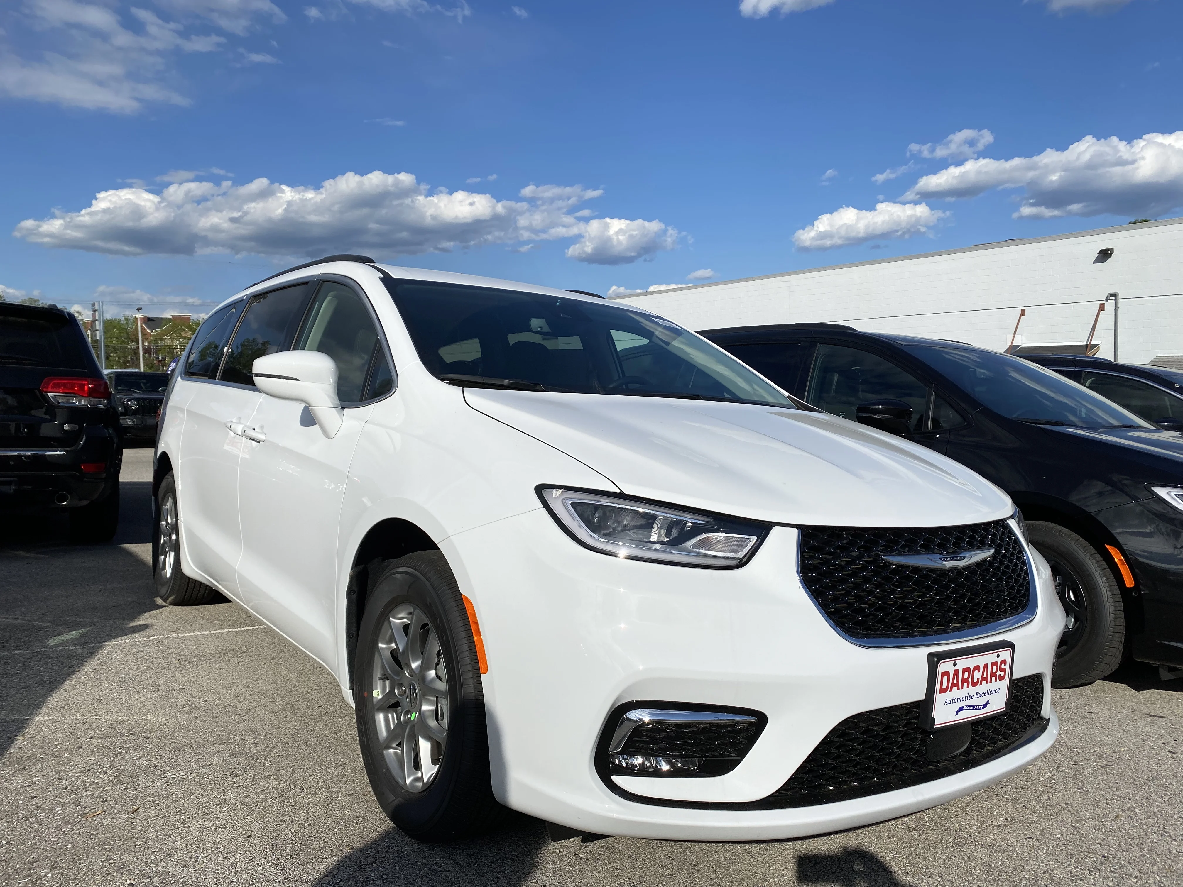 White Chrysler Pacifica minivan, current generation, front three-quarter view with a black mesh grille, in a dealership lot.