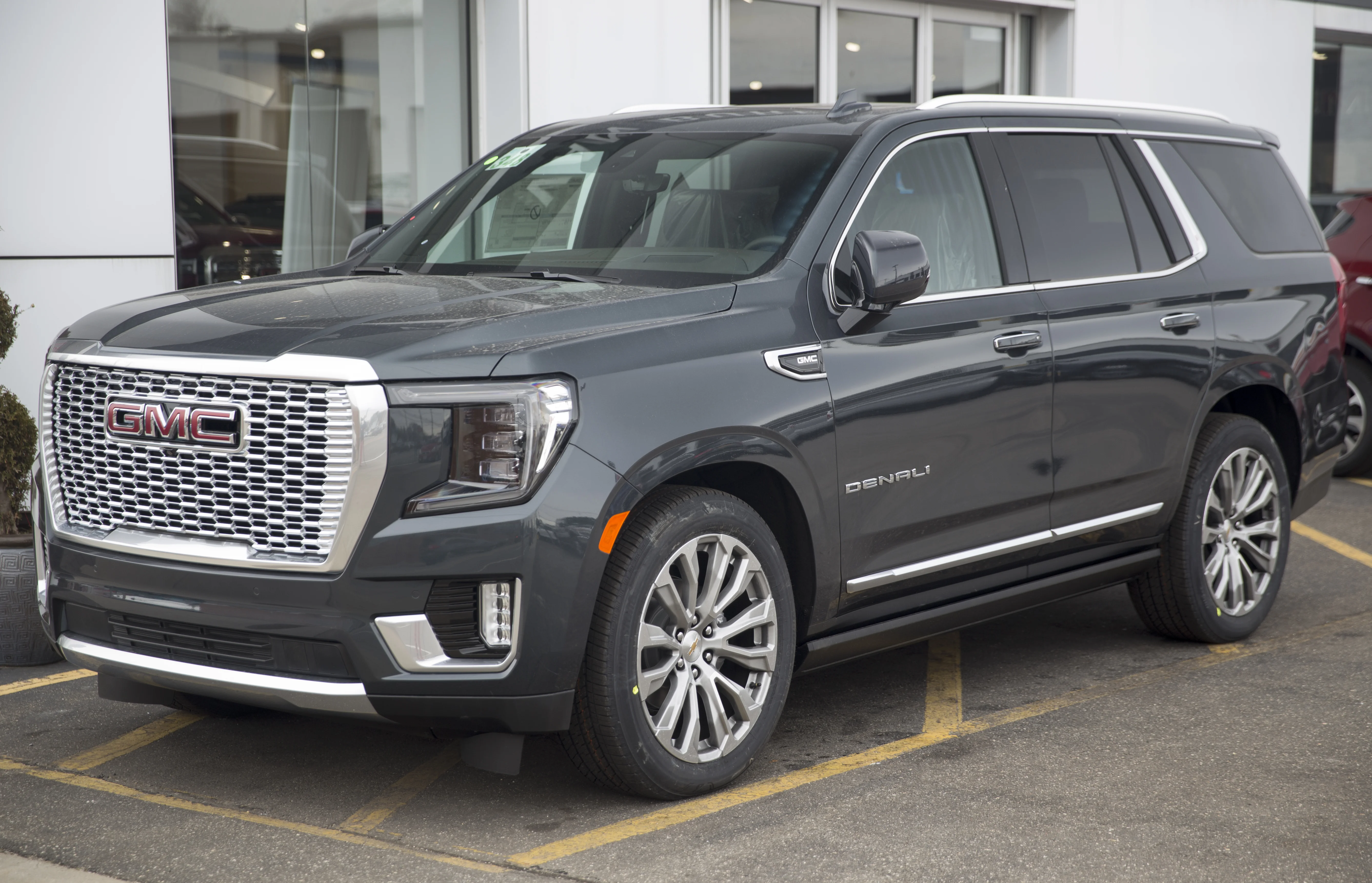 Dark gray metallic GMC Yukon Denali full-size SUV, front three-quarter view with a chrome grille and polished alloy wheels at a dealership.