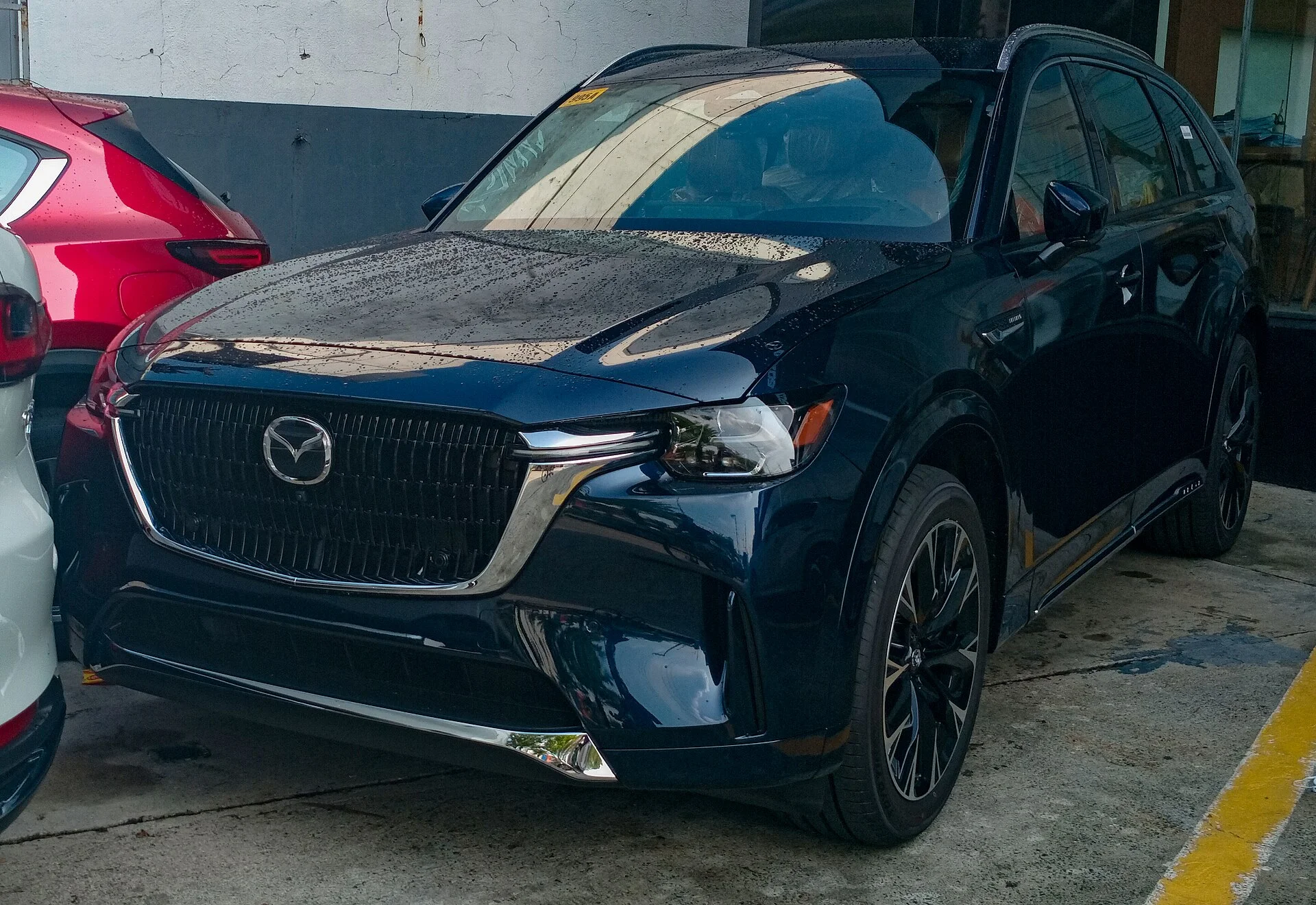 Dark blue Mazda CX-90 three-row SUV, front three-quarter view with a chrome grille and machined-alloy wheels.