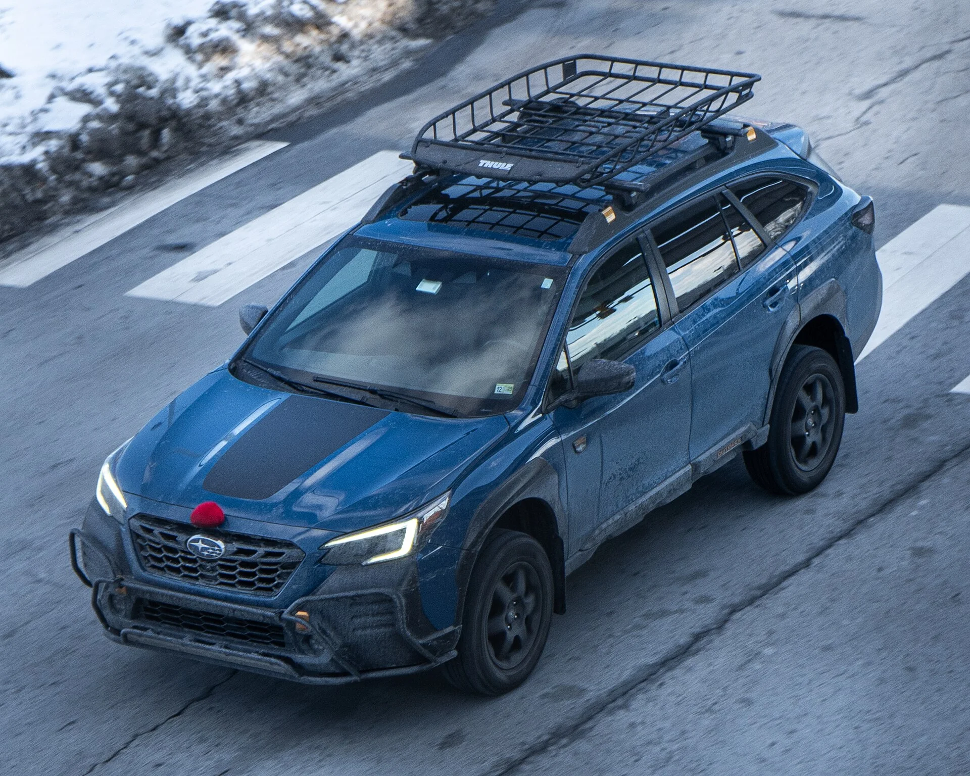 Blue Subaru Outback with a roof cargo basket mounted, front three-quarter overhead view