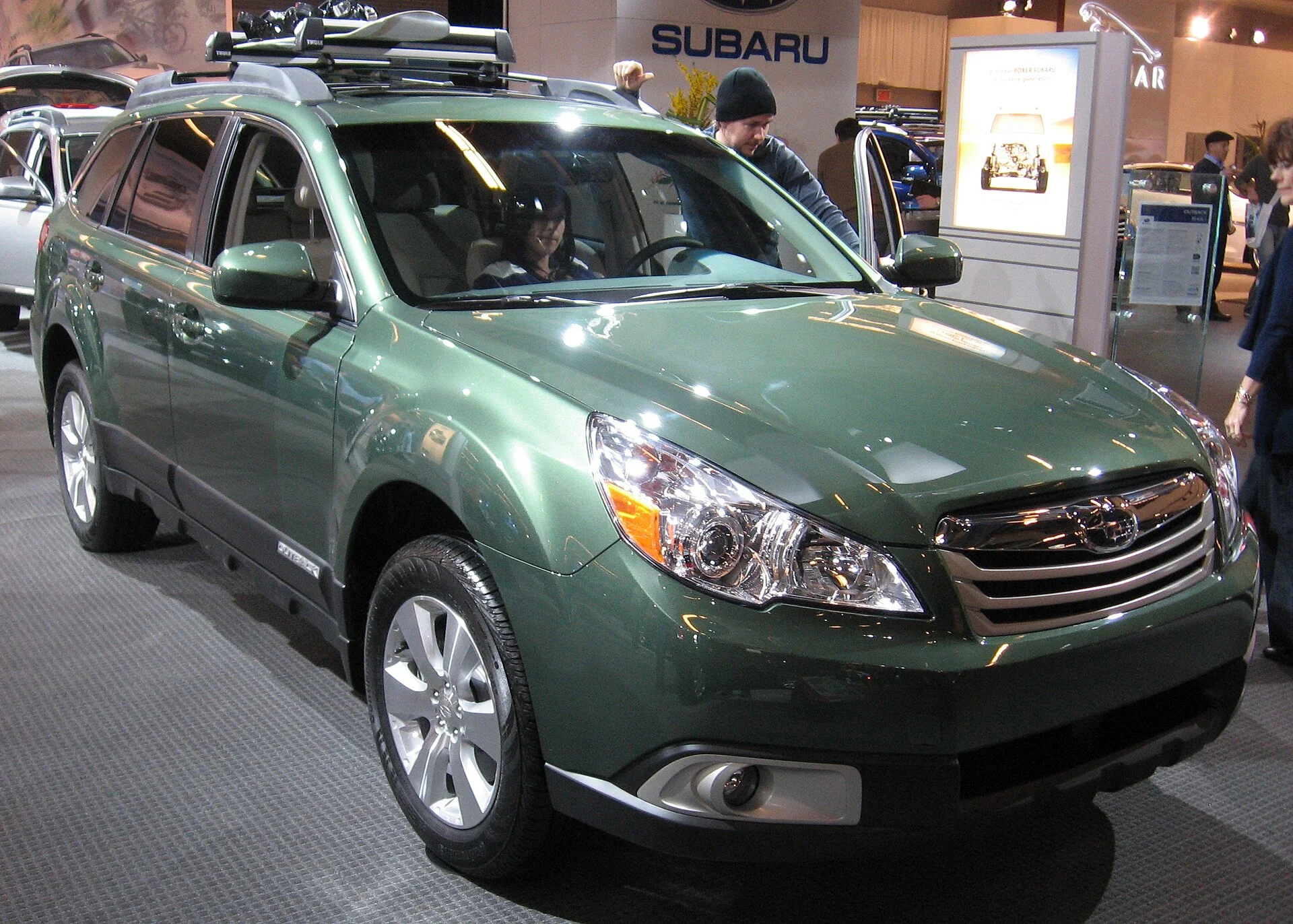 Green Subaru Outback with roof rails, front three-quarter view