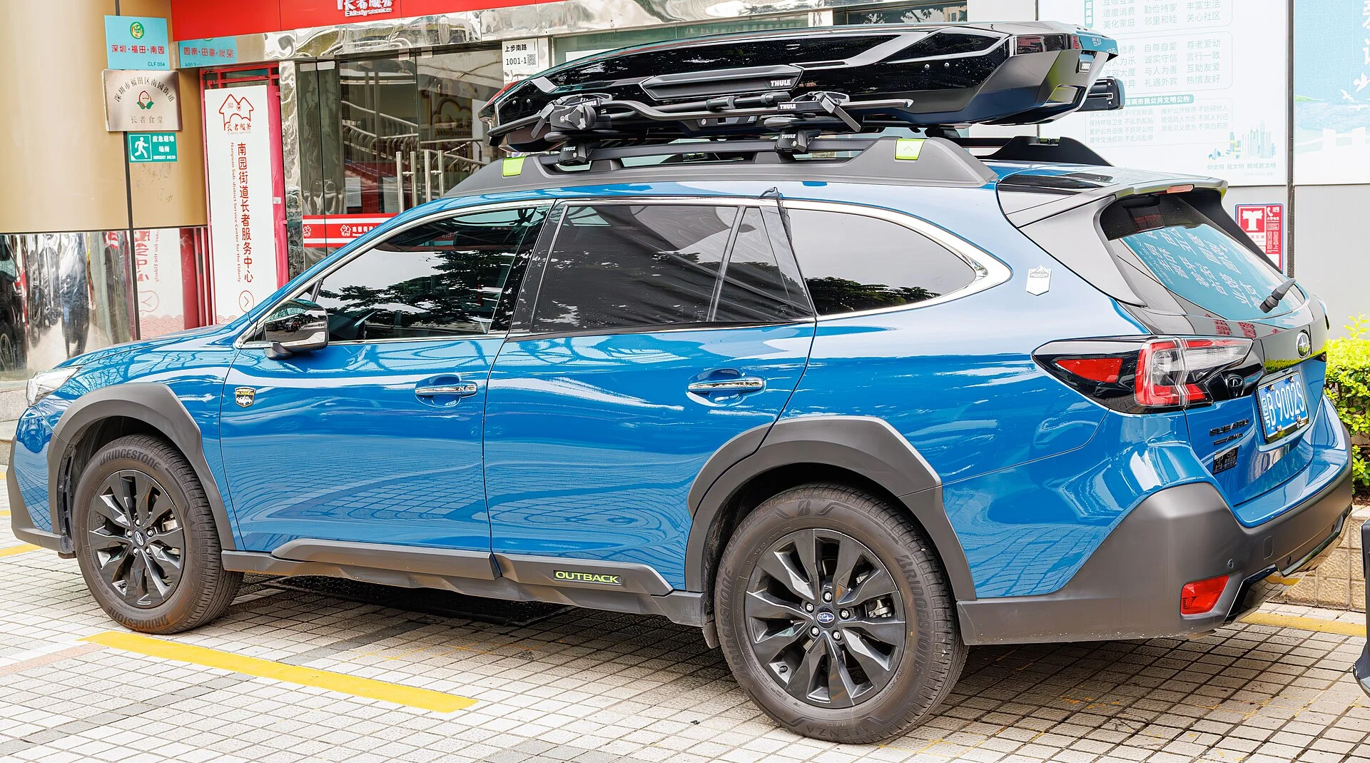 Subaru Outback (6th generation) in blue with a roof cargo box, rear three-quarter view