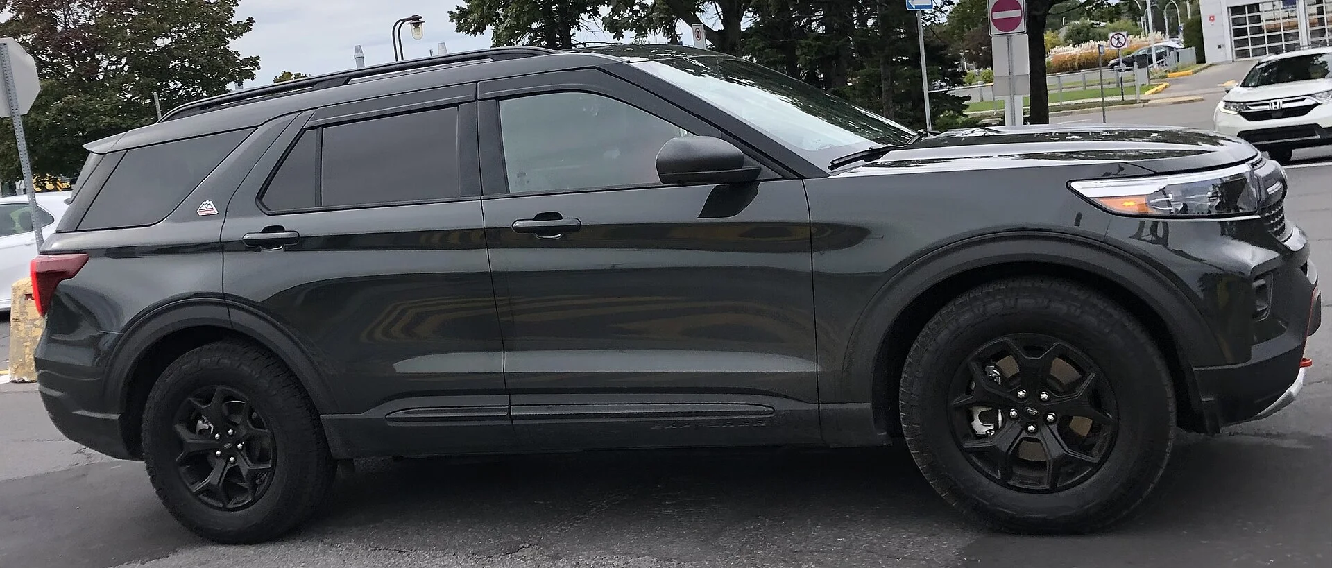 Black Ford Explorer Timberline SUV with black off-road wheels and roof rails, side profile view in a parking lot.