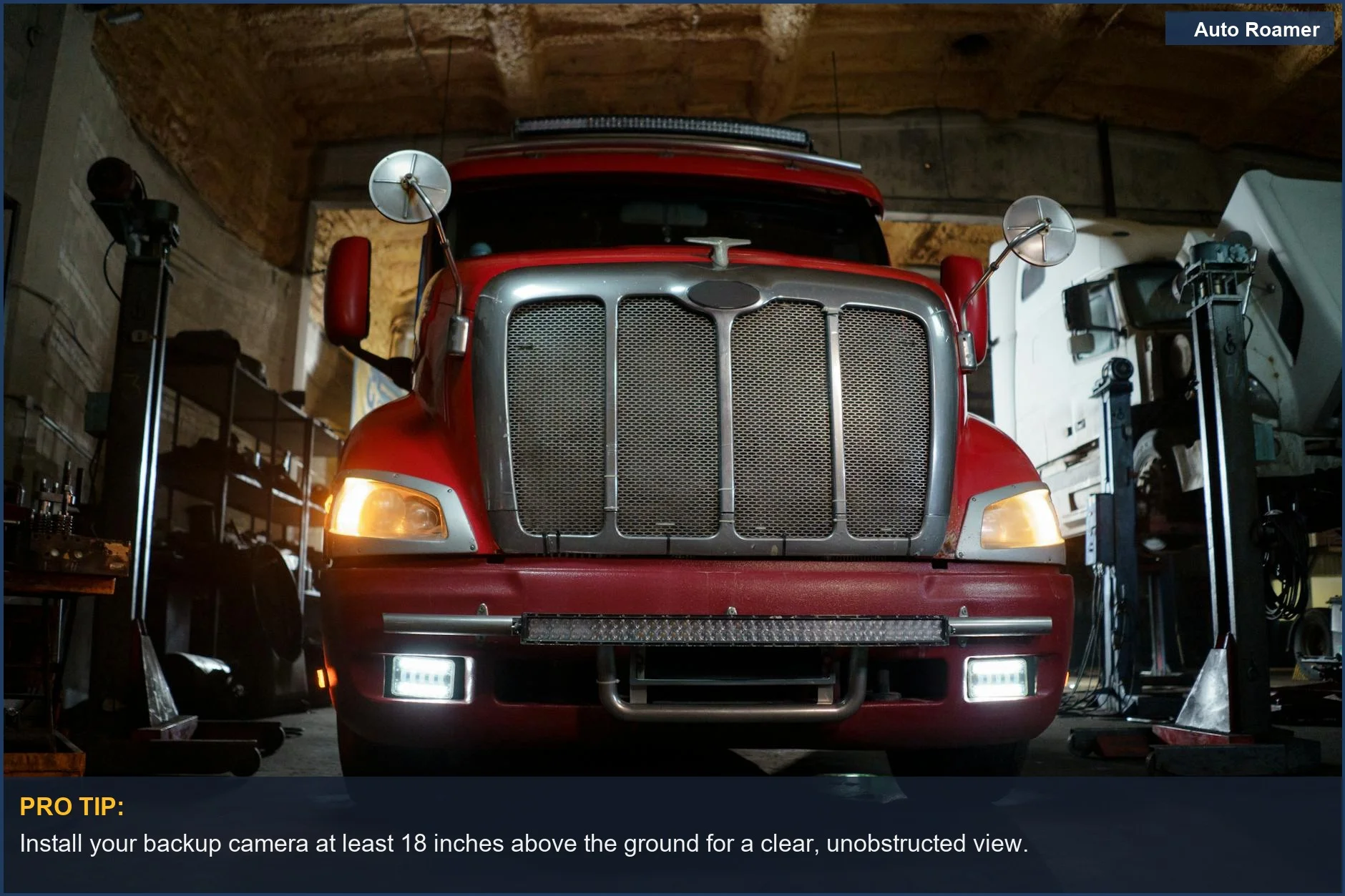 Front view of a red truck's grill and headlights in a repair shop.