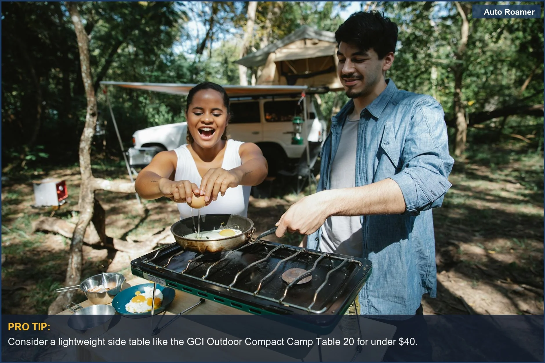 Couple cooking breakfast on a compact camping table near a car and tent.