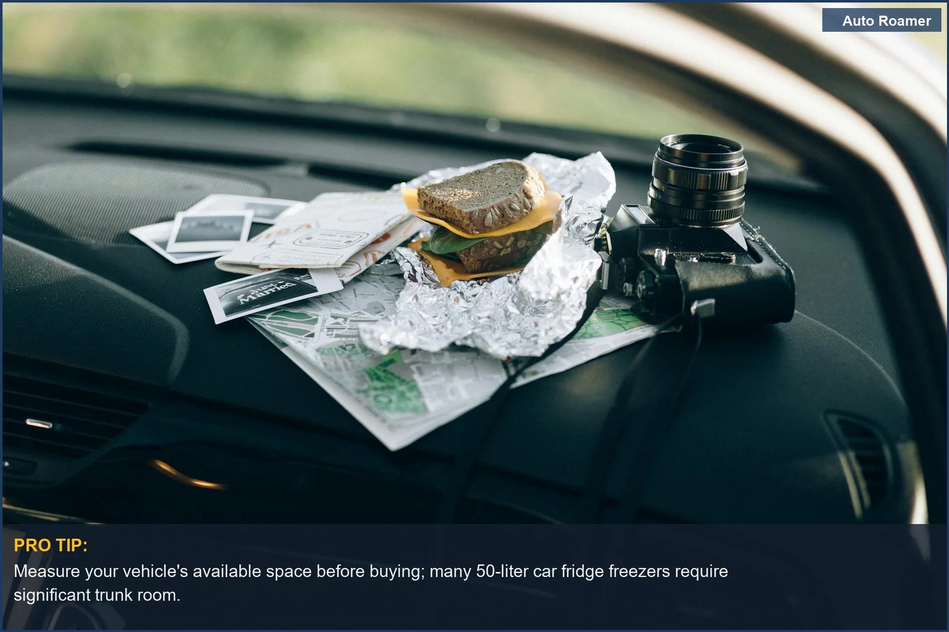 Close-up of travel preparation on a car dashboard, including a camera, foil-wrapped sandwich, and maps.