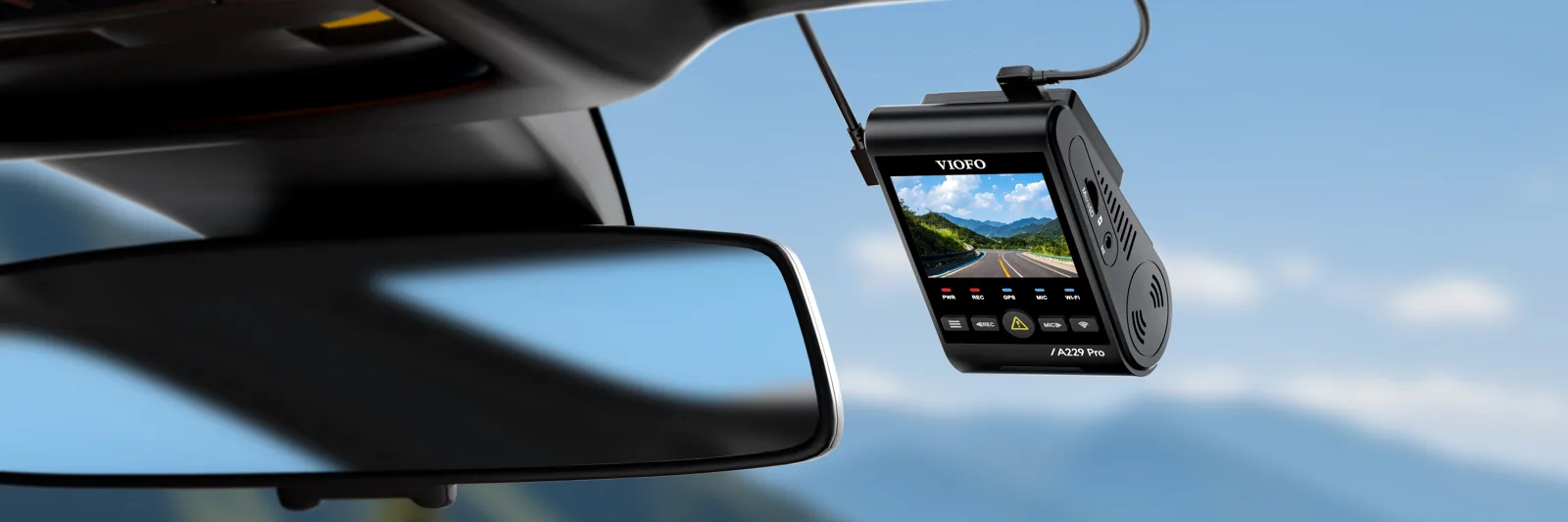 VIOFO A229 Pro dash cam mounted on a car windshield beside the rearview mirror with a bright mountain sky behind, its screen showing a live road view, the VIOFO unit compared against the BlackVue Elite 10