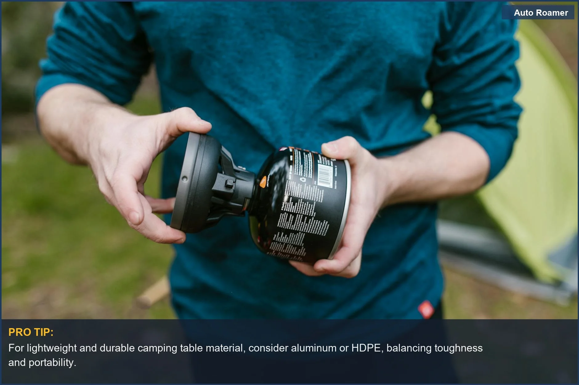 Man setting up a portable camping stove near a tent in a grassy campsite.