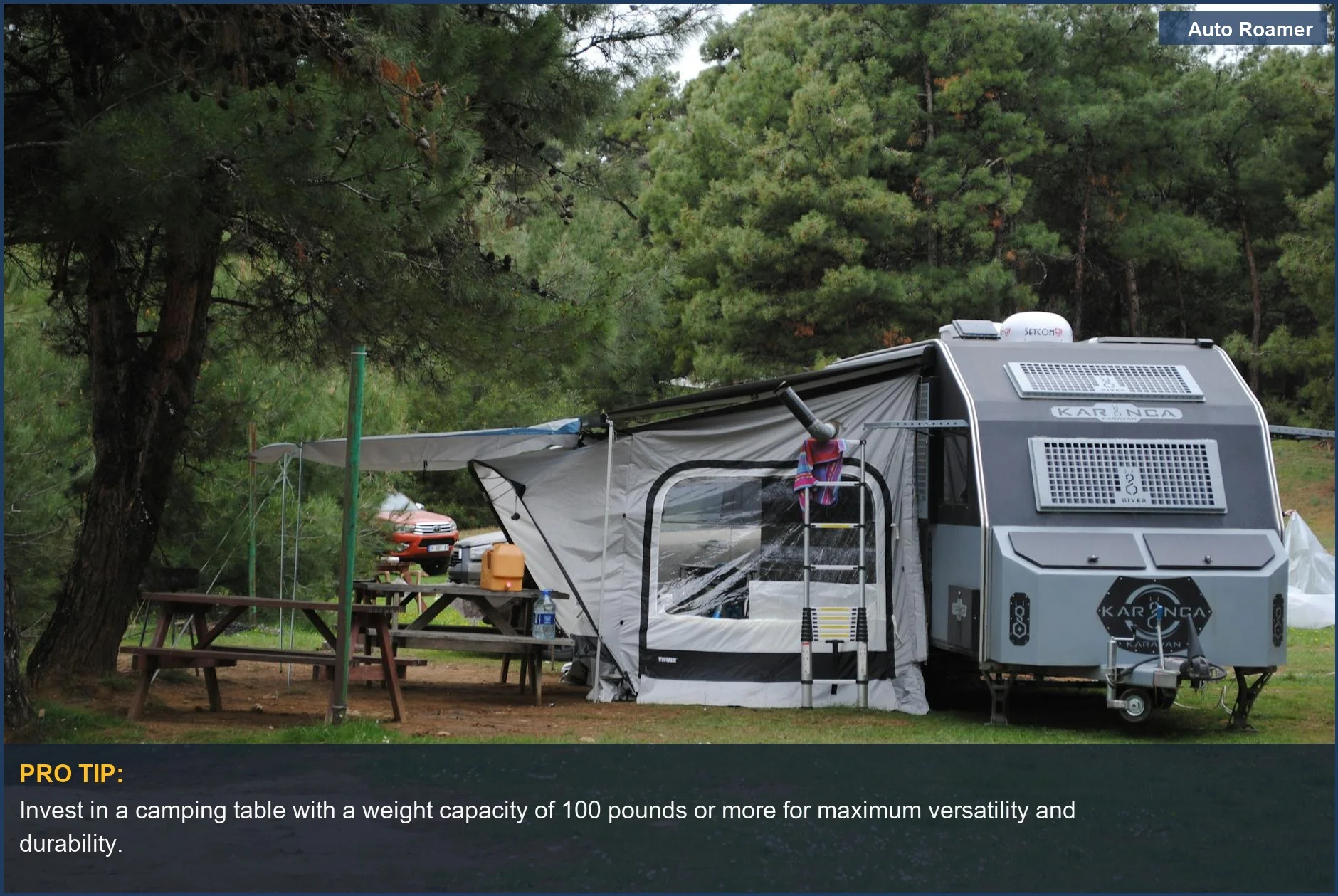 Tranquil forest campsite with a caravan, lush greenery, and sturdy wooden tables, ideal for car camping.