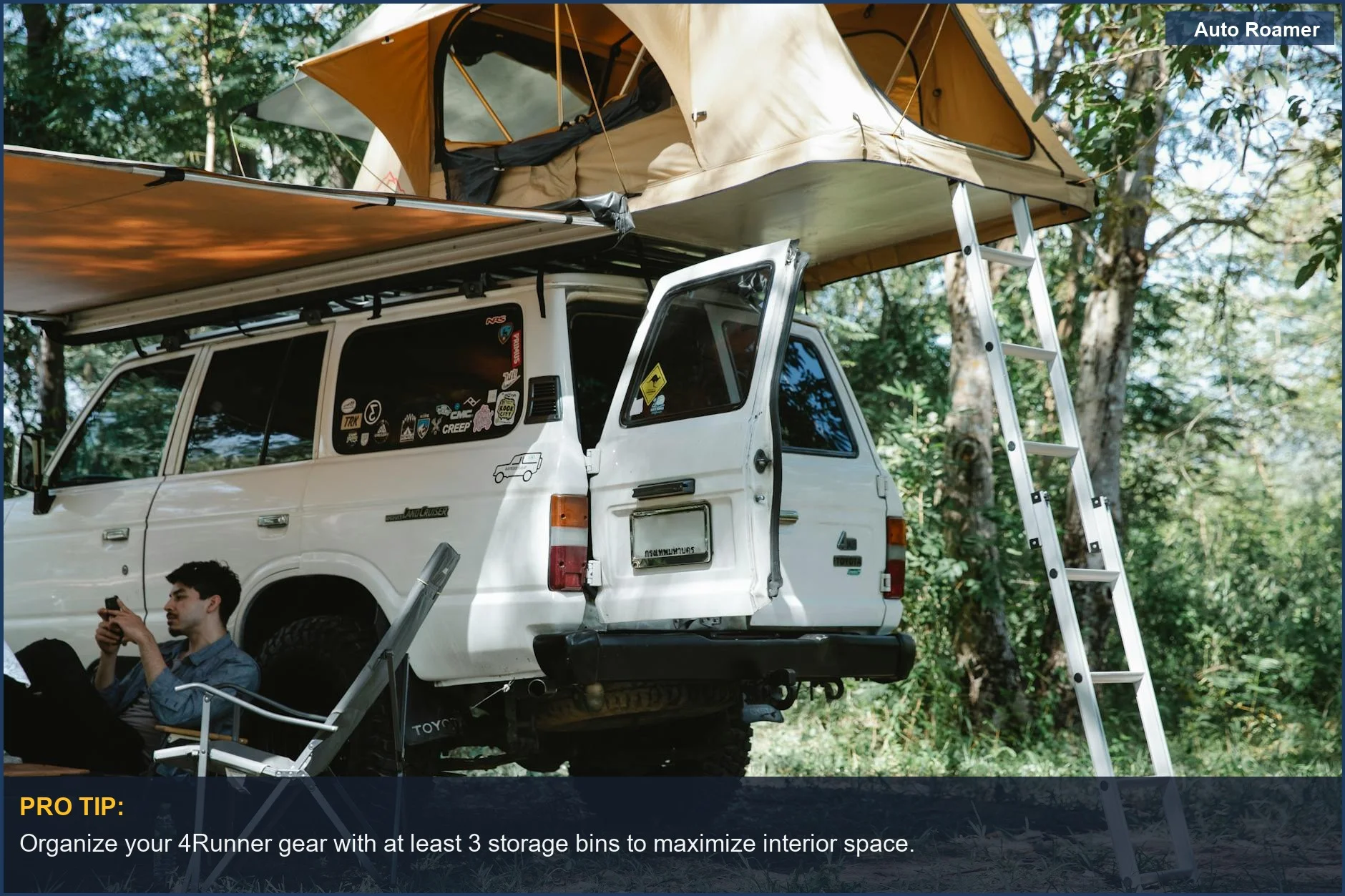 Hombre relajándose con el teléfono junto a un 4Runner y una tienda de techo en un bosque, demostrando la comodidad de dormir en 4Runner.