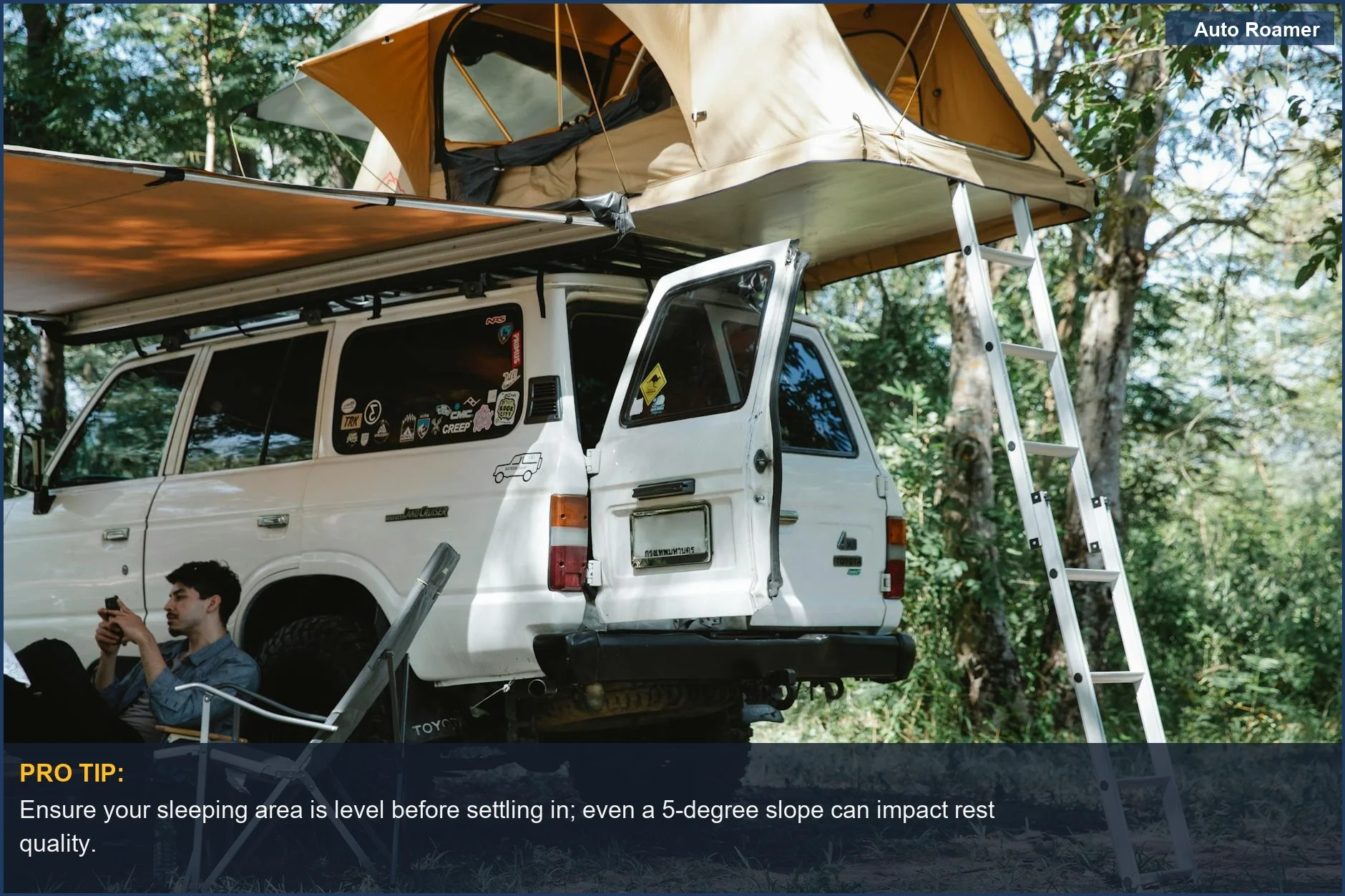 Man relaxing with a smartphone next to an offroad vehicle and rooftop tent in a forest, illustrating comfortable car camping.