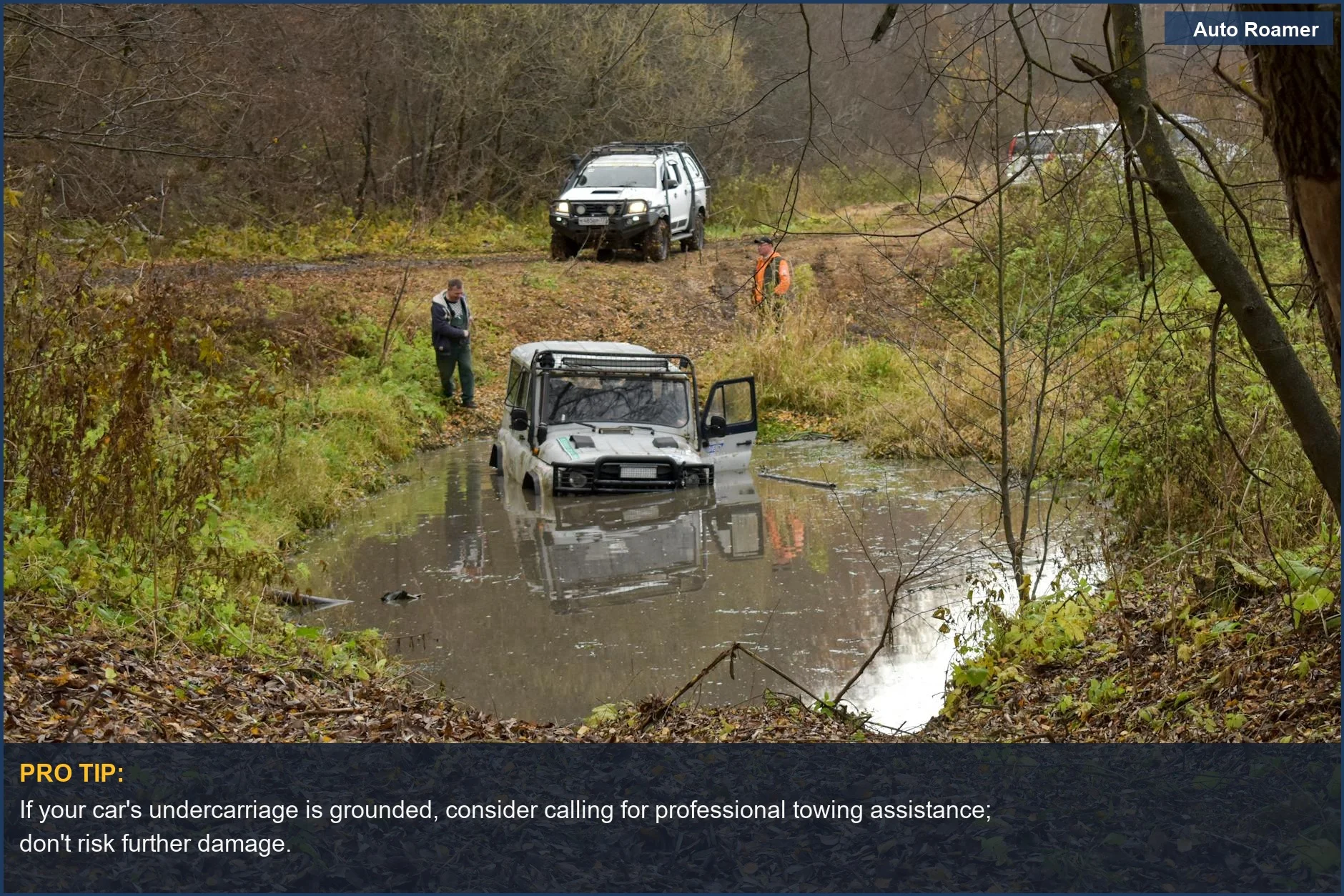 SUV hoisted in muddy water on a forest trail, people surrounding it, a visual of a car stuck in mud.