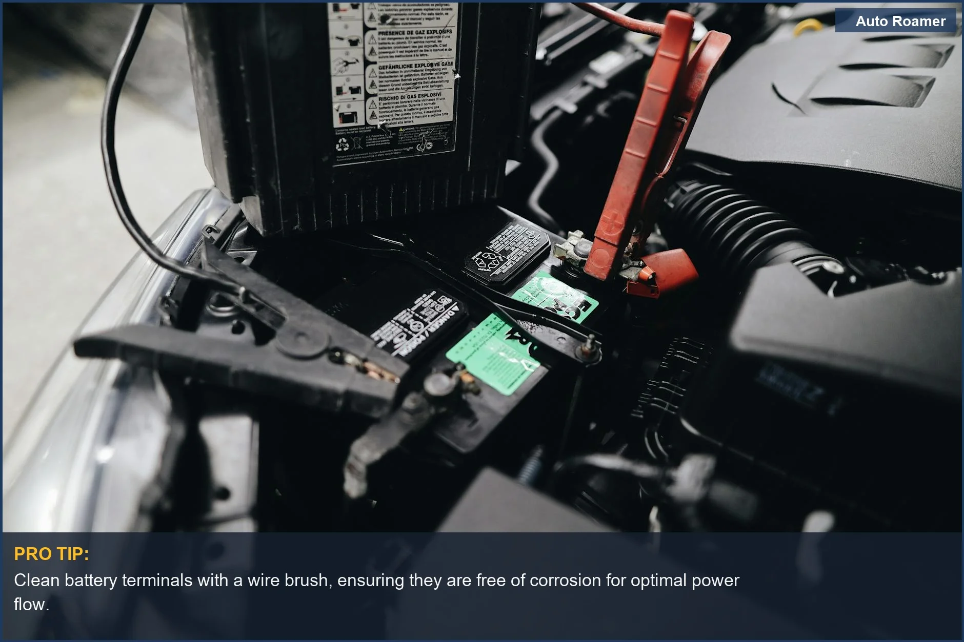 Close-up of car battery terminals being jump-started with red and black cables in an engine bay.