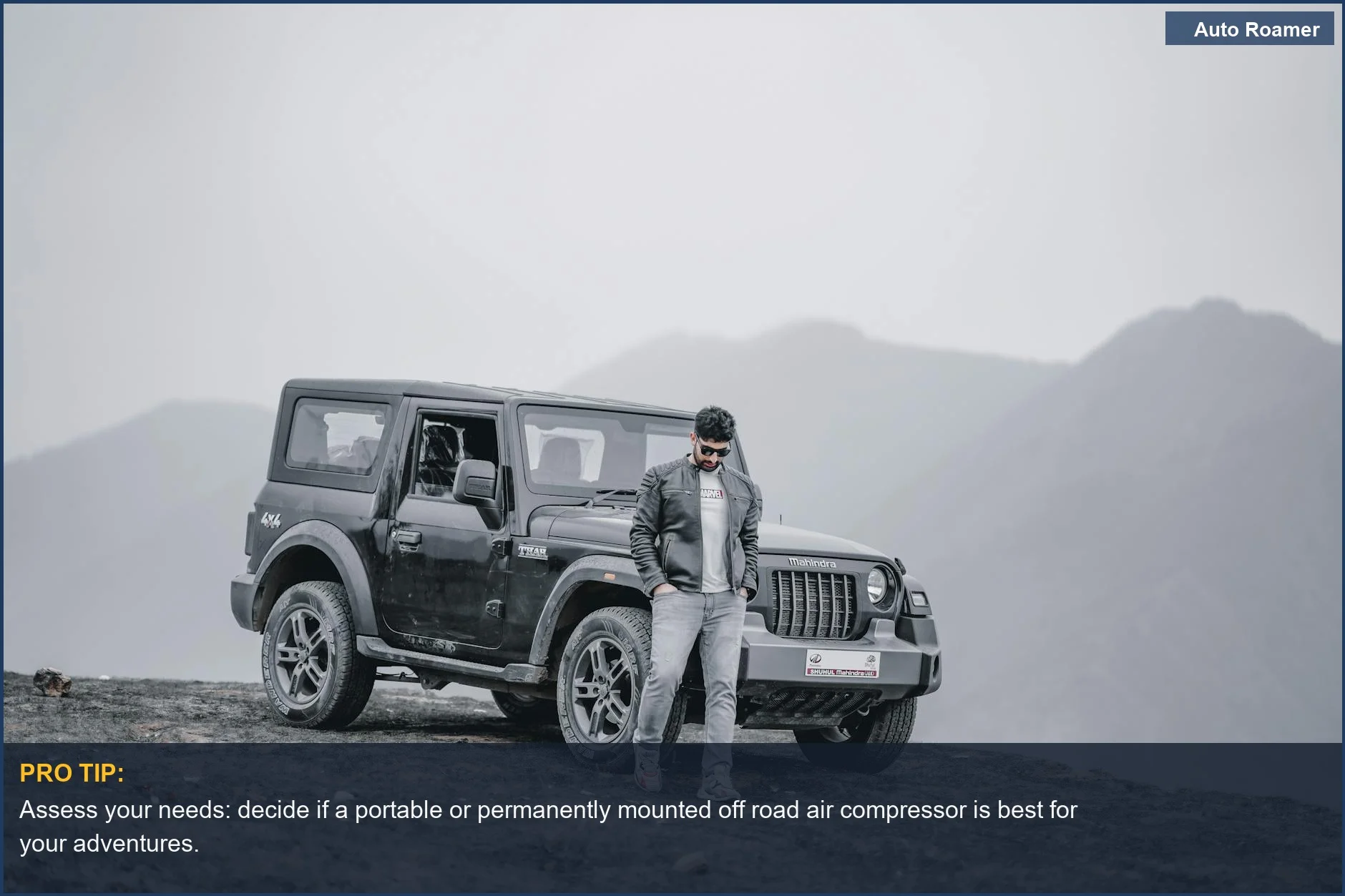Man with off road air compressor next to a Mahindra Jeep in mountains, ready for vehicle tire inflation.