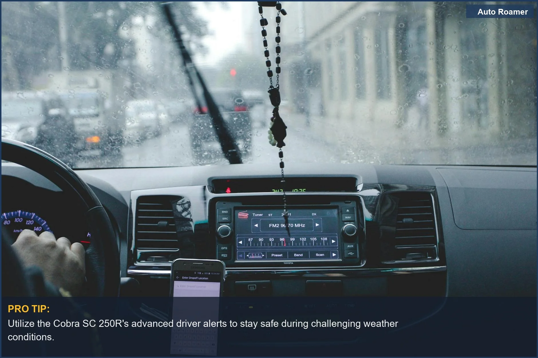 Navigating a rainy cityscape from a car's interior, highlighting the dashboard and a phone, relevant for Cobra SC 250R driver alerts.