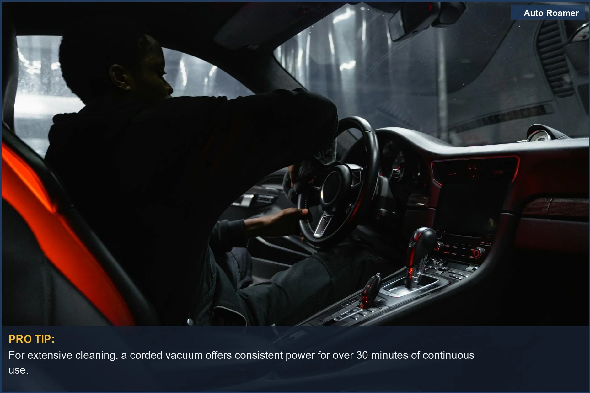 African American man focusing on cleaning car dashboard and steering wheel with a corded vacuum.