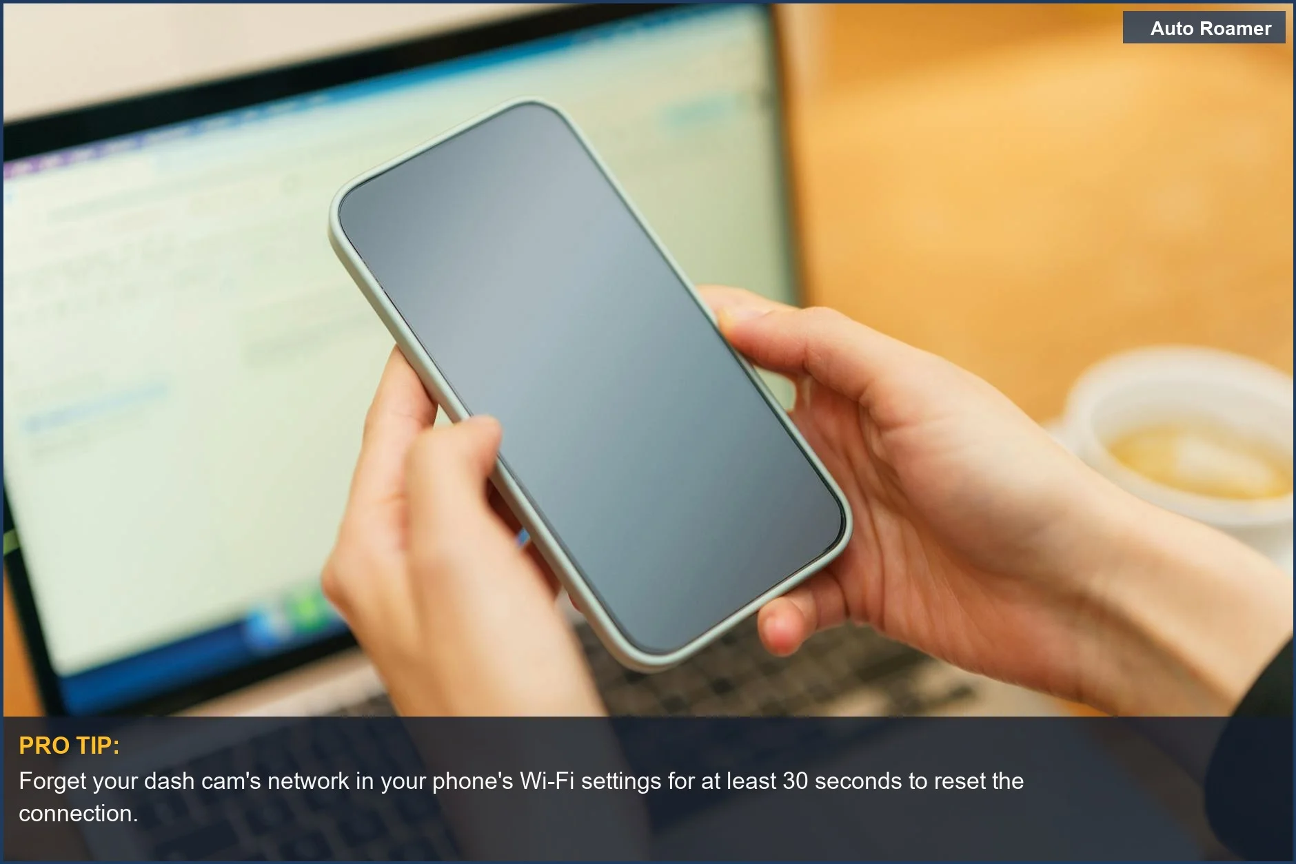 Person holding a smartphone over a laptop, suggesting troubleshooting steps for a dash cam that won't connect to Wi-Fi by forgetting networks.