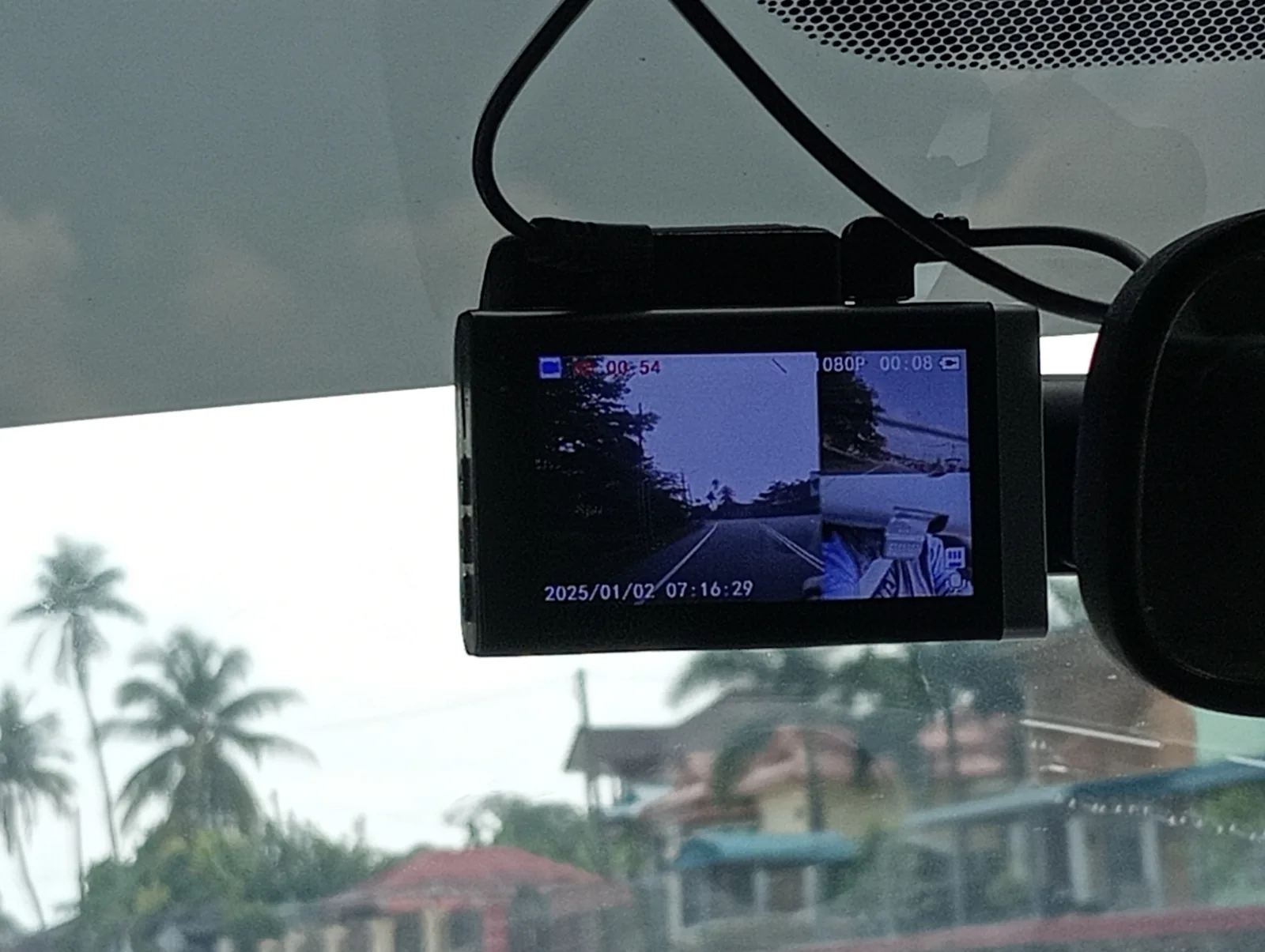 A windshield-mounted dash cam with its screen switched on, showing a live split-screen road view and the on-screen date and time stamp 2025/01/02 07:16:29, illustrating how a dash cam displays its clock.