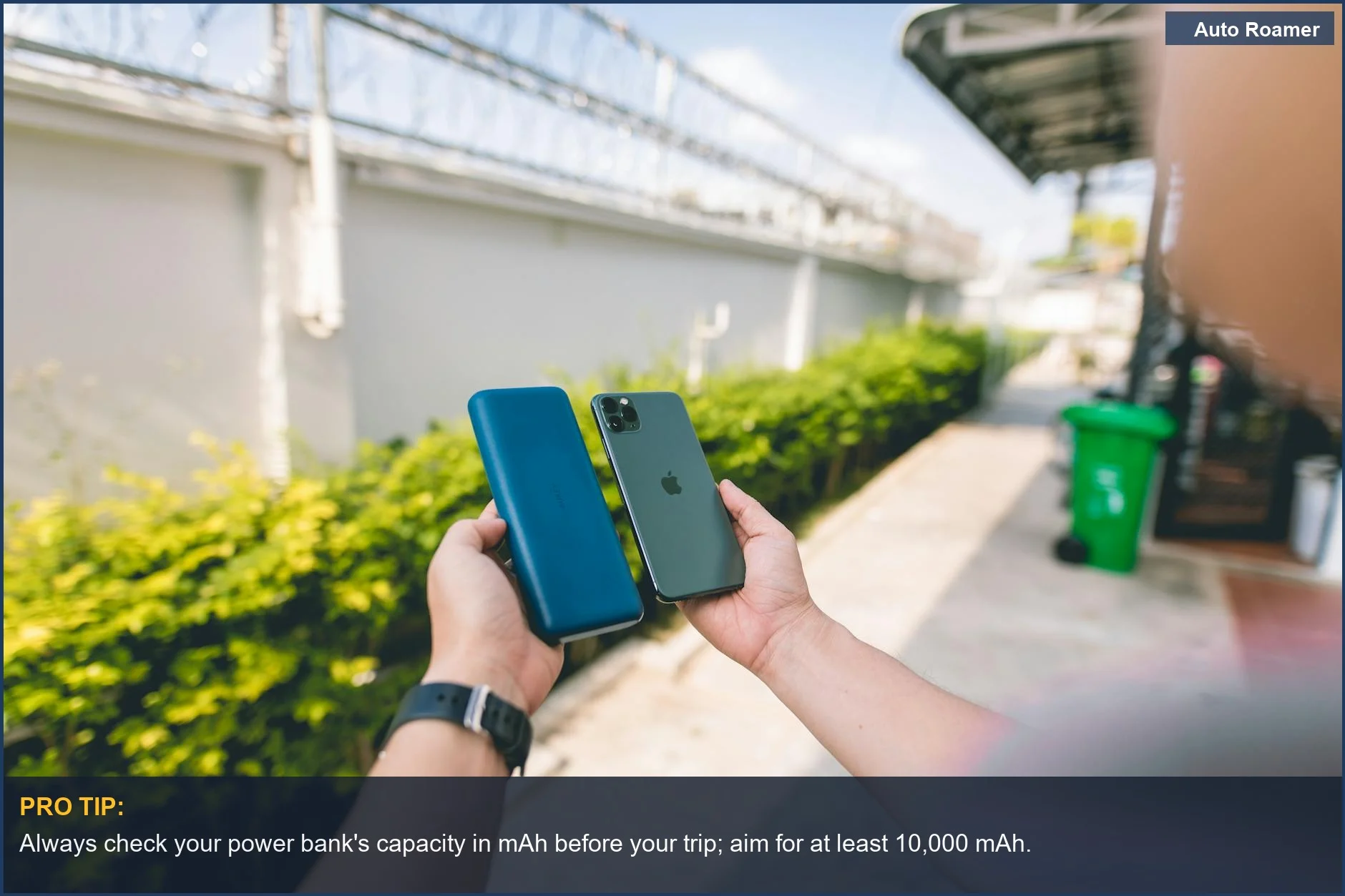 Hands holding a smartphone and power bank outdoors, ensuring portable power for road trip electronics.