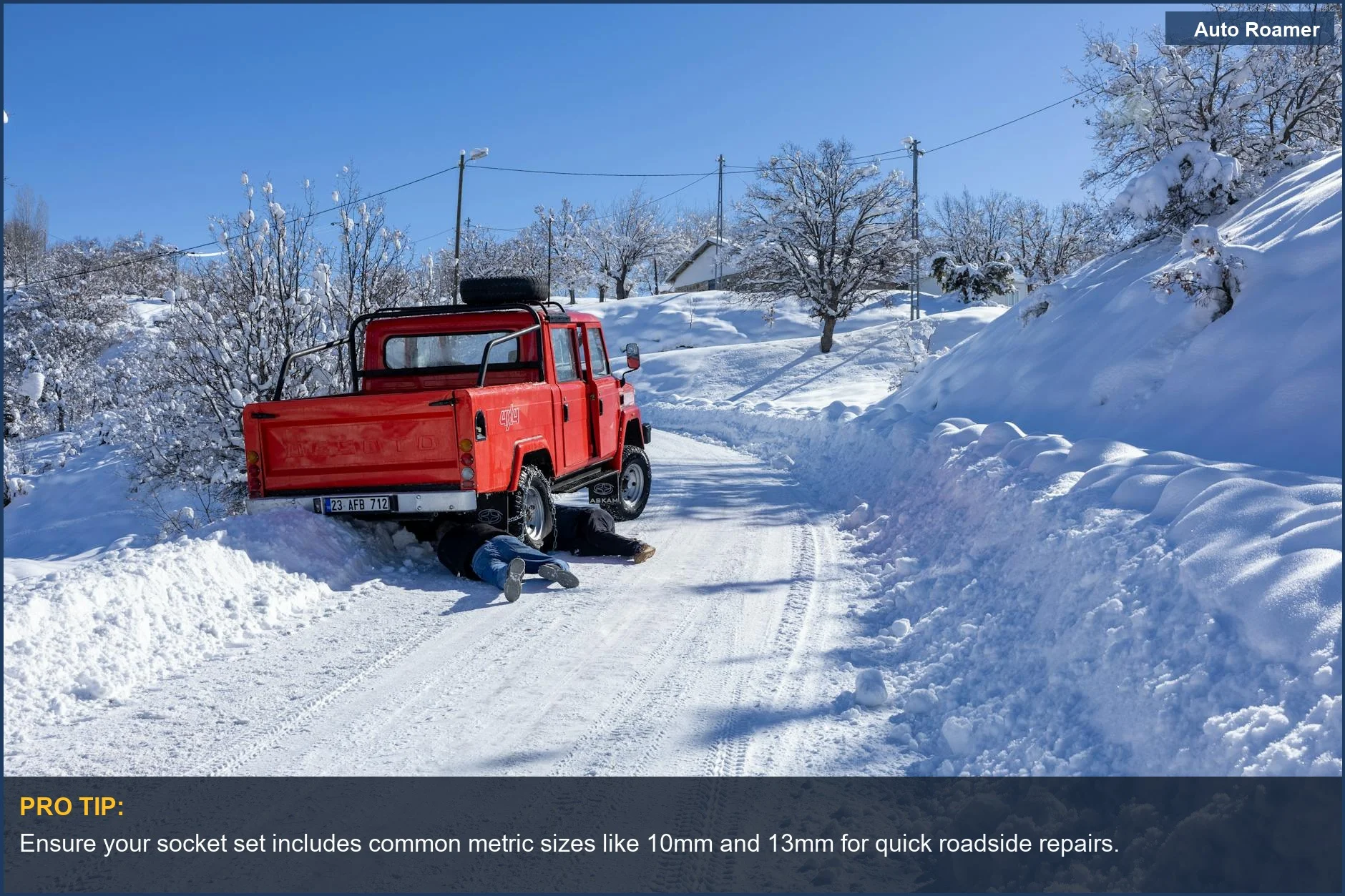 Mechanic performing roadside repair on a red truck with a socket set in snowy conditions.