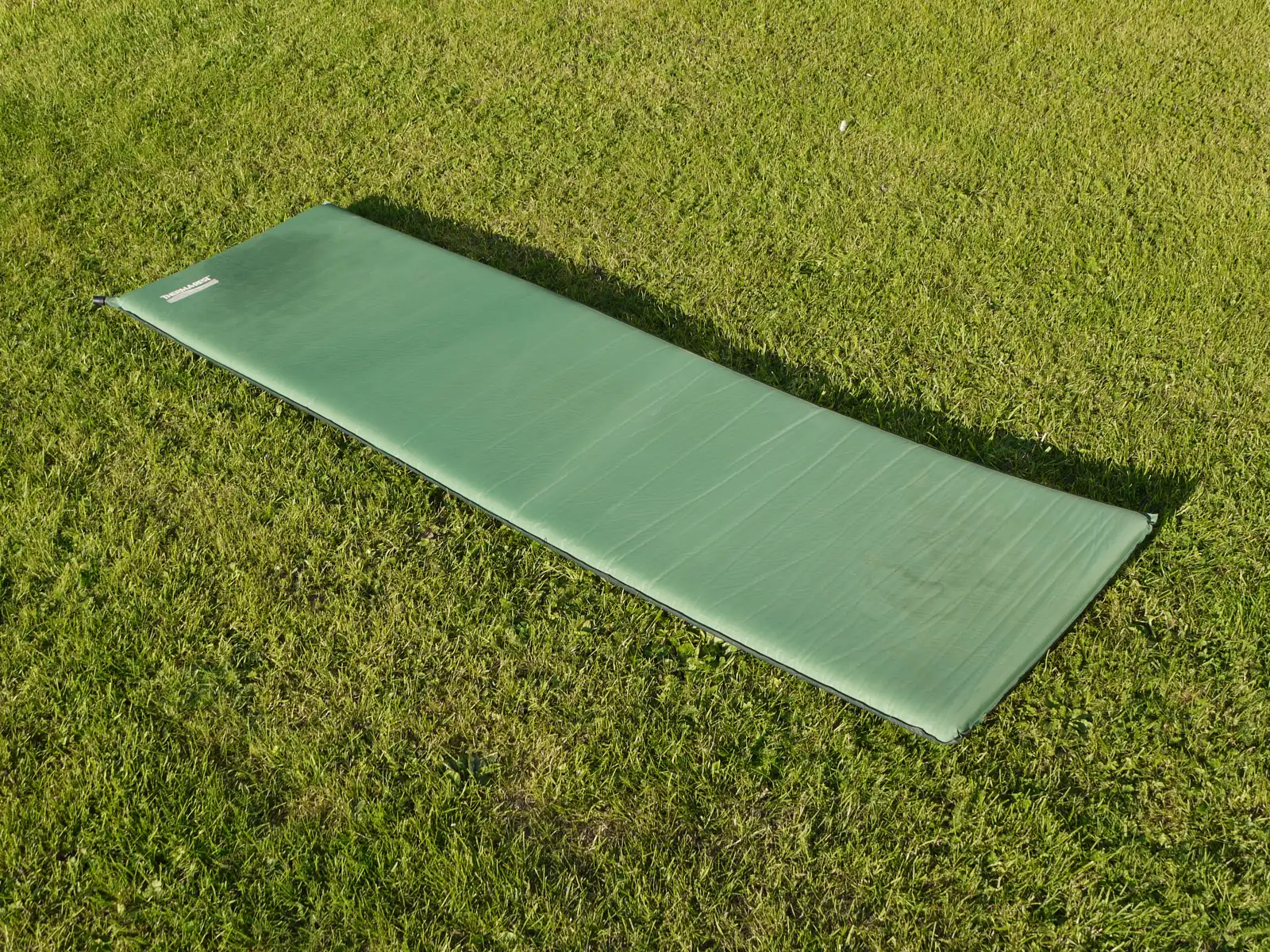 A green Therm-a-Rest self-inflating sleeping pad laid out on grass, one of the two car-camping pads this guide compares