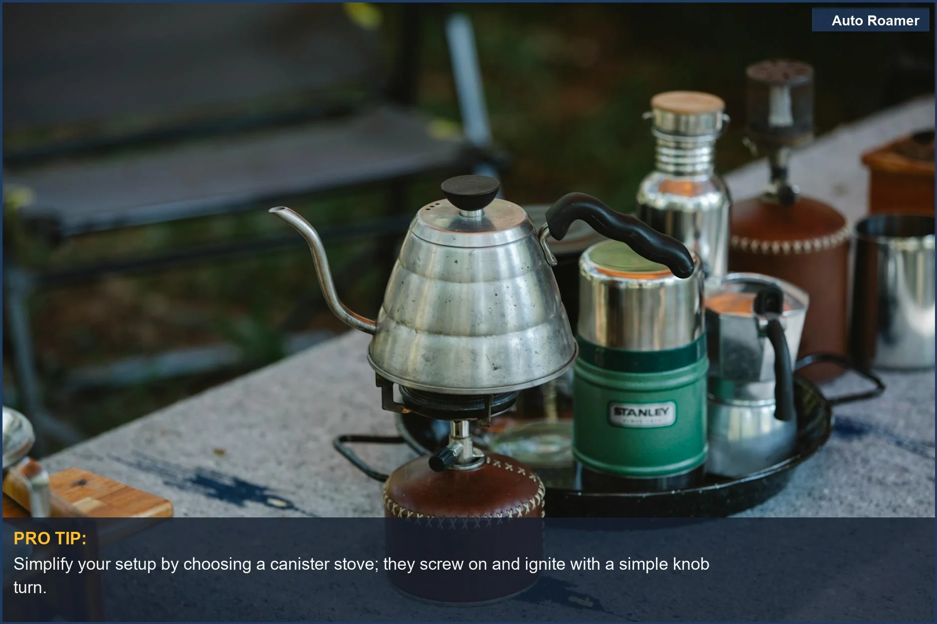 High angle of a metal coffee kettle on a portable camping gas stove with utensils.