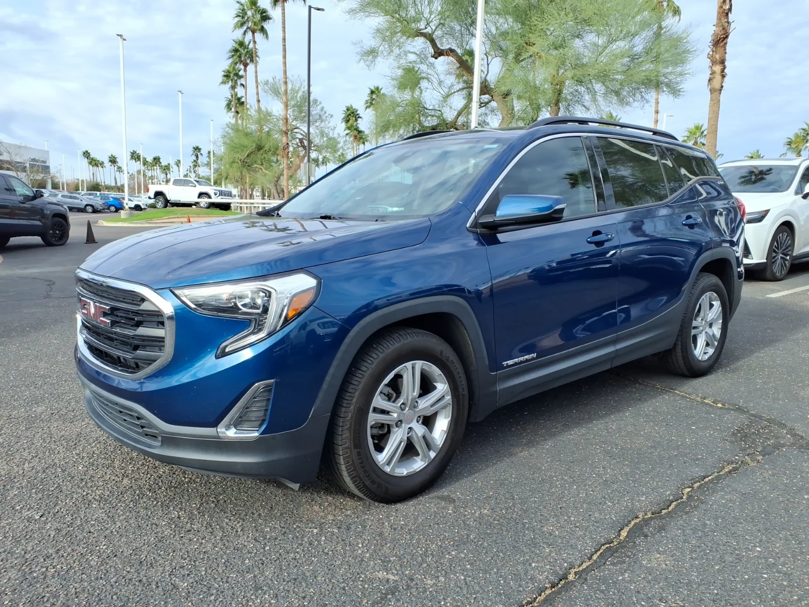 A blue GMC Terrain SLE compact SUV in a front three-quarter view in a parking lot, illustrating the crossover this gear guide outfits for camping.