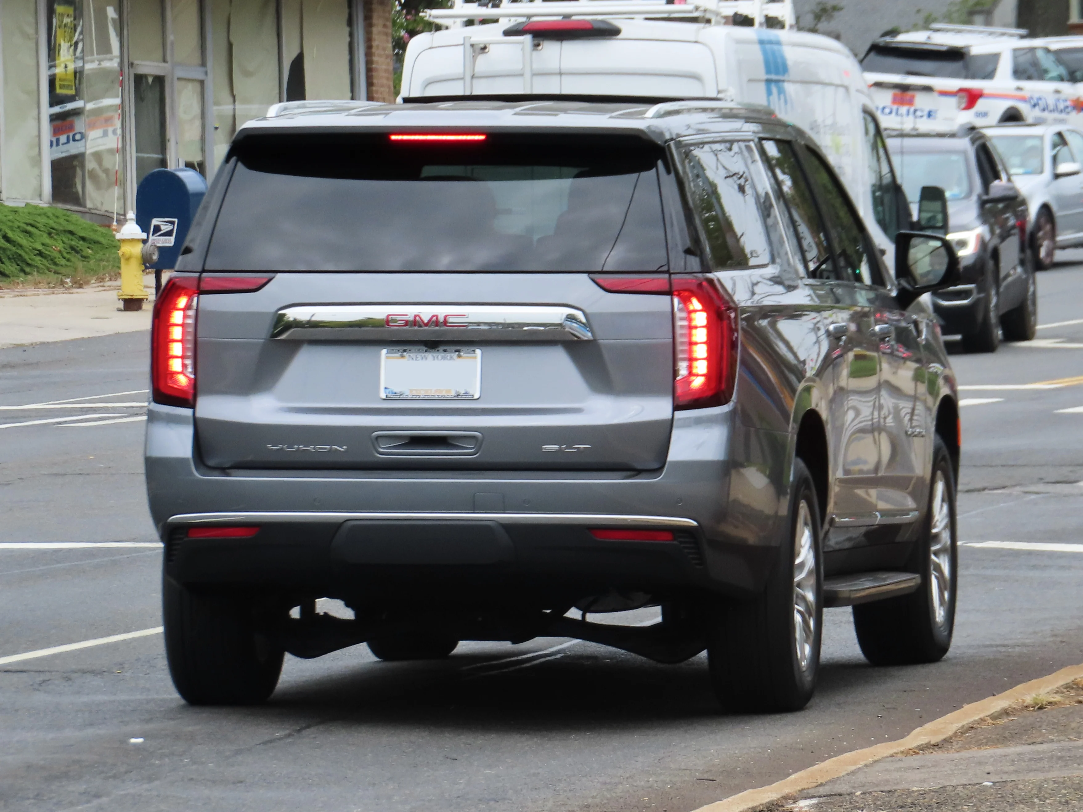 A grey 2021 GMC Yukon XL SLT full-size SUV seen from the rear three-quarter, the tailgate and long body that set its cargo length with the seats folded.